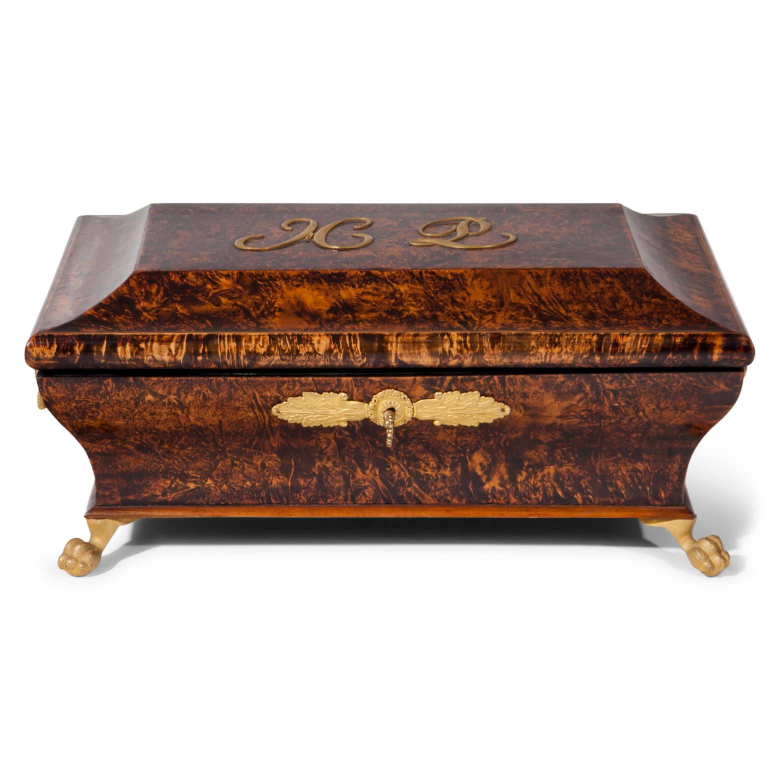 French Charles X burl wood box, standing on bronze ball-and-claw feet. The body is slightly curved and the lid shows the monogram ML. The key exists.