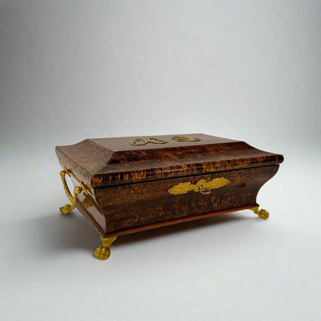 A French Charles X burl wood box, crafted around 1820. The box stands on elegant bronze ball-and-claw feet.
The body is subtly curved and the lid features the monogram ML. The original key is present.


