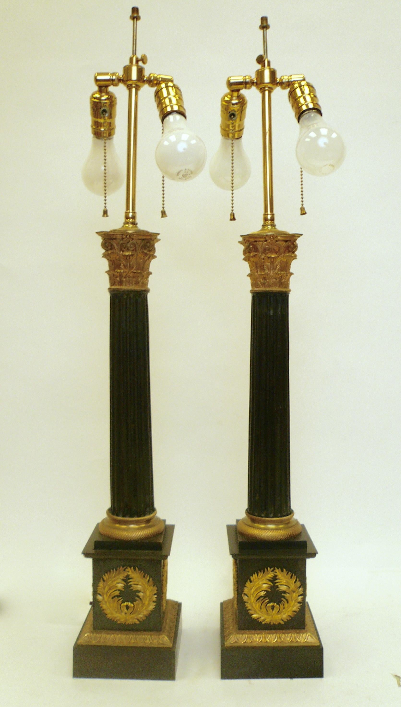 Originally oil lamps, this pair of bronze columnar form lamps feature gilt bronze classical wreaths, and Corinthian capitals.