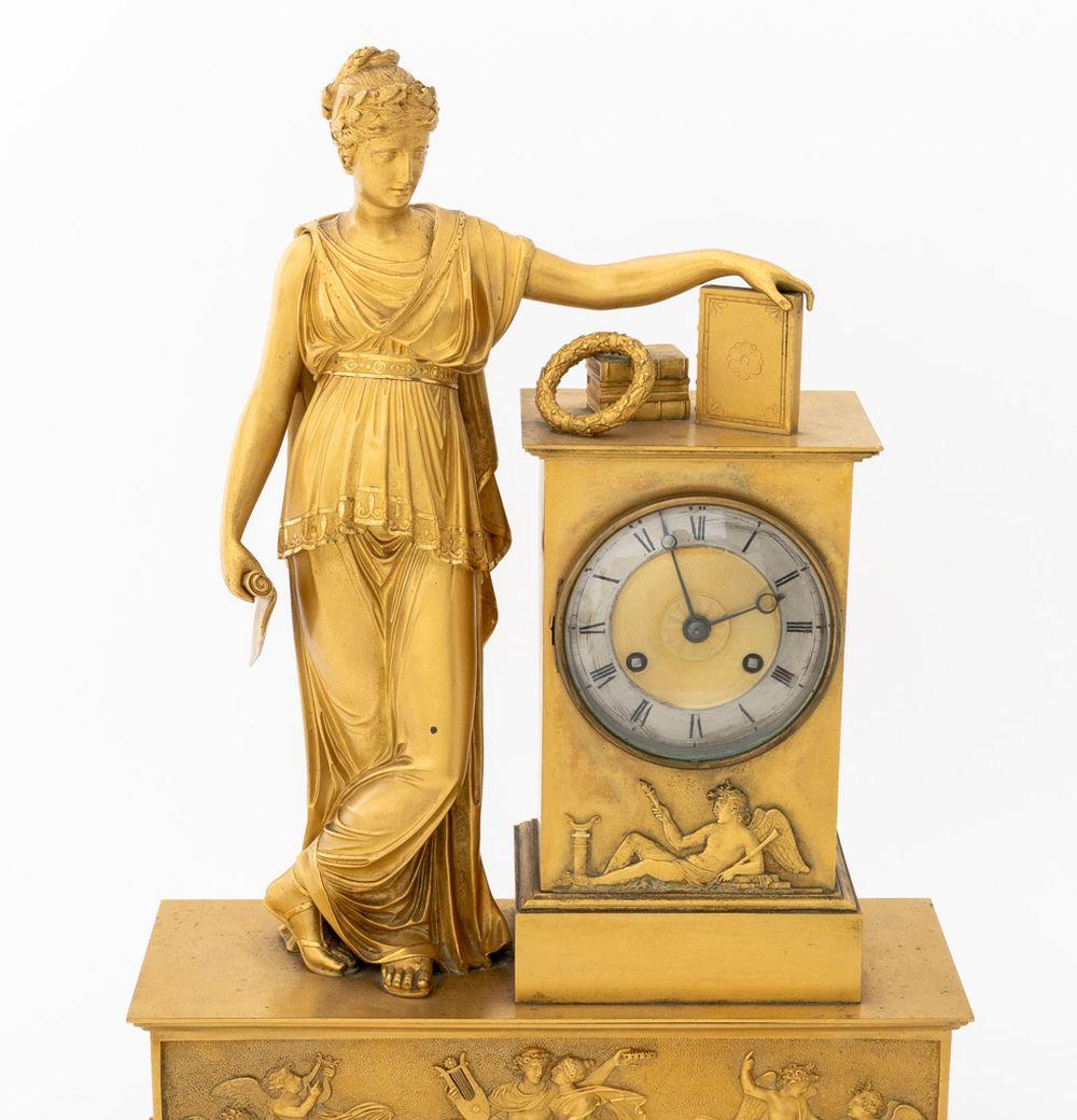 Pendule de cheminée en bronze doré Charles X, vers 1830, représentant Clio, muse de l'Histoire, debout à côté d'un piédestal, centré par un cadran argenté, le mouvement sonnant sur une cloche, sur un socle rectangulaire moulé avec une frise d'Apollo