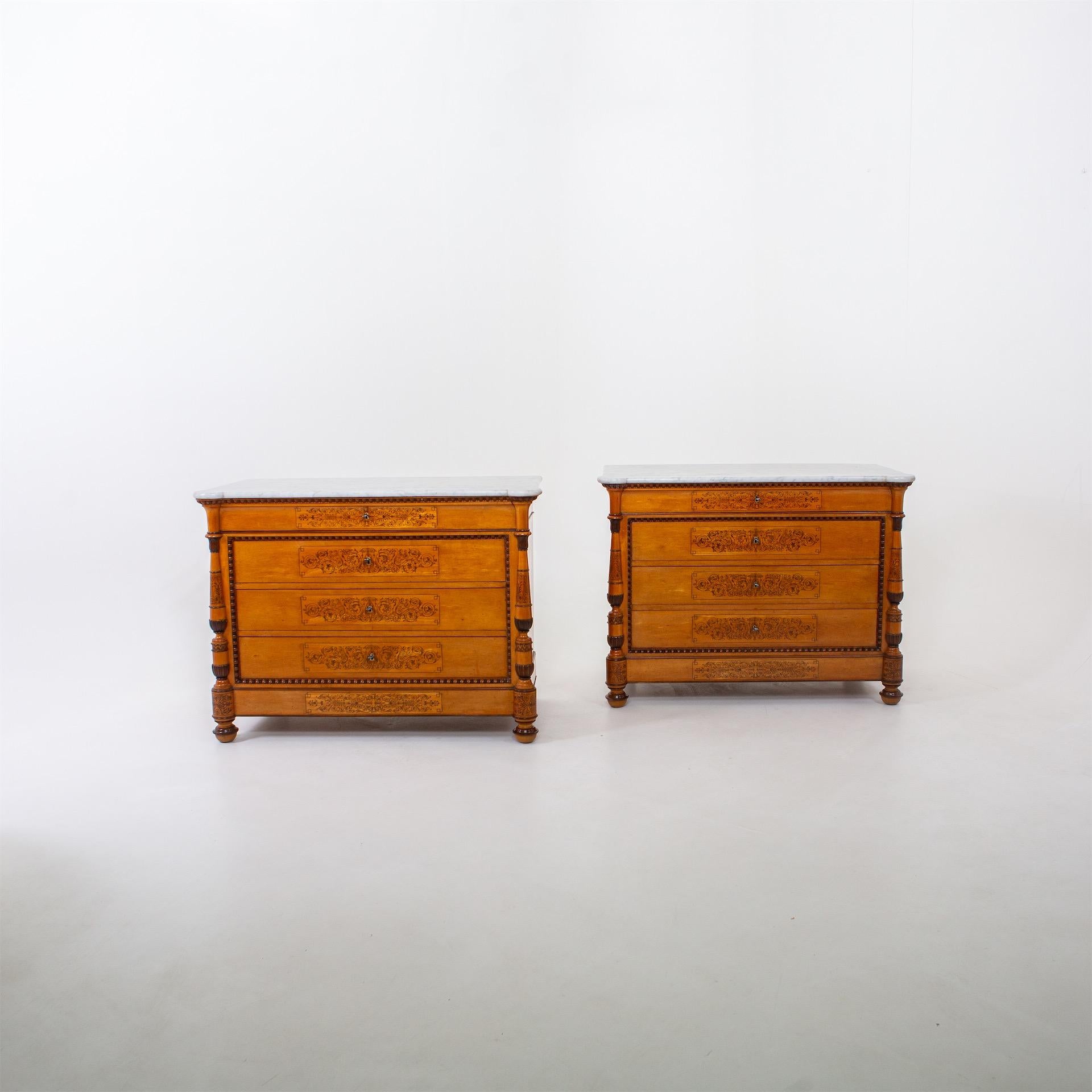 Pair of large Charles X chests of drawers with four drawers in maple and poplar, veneered and solid. The bodies with balustered columns at the corners stand on profiled ball feet and are covered with light grey marble slabs. The fronts are decorated