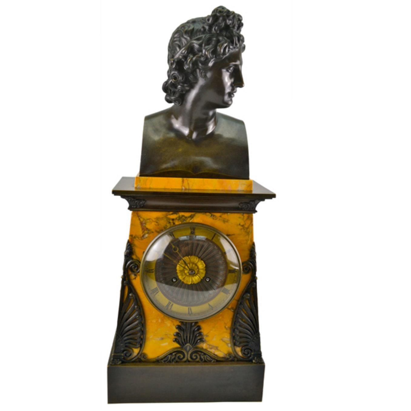 Un bel exemple de pendule de cheminée d'époque Empire français, vers 1830. Le boîtier rectangulaire à gradins est en marbre jaune de Sienne et est décoré sur le dessus et le dessous de bronze patiné. Au sommet du boîtier de l'horloge trône une tête