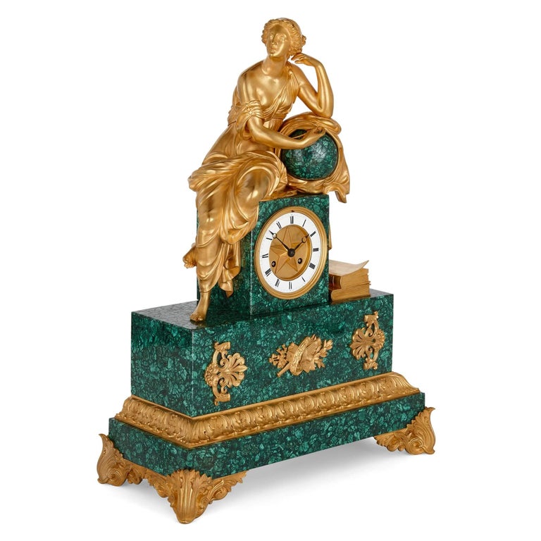 Charles X period gilt-bronze and malachite sculptural mantel clock.
French, c.1830.
Measures: height 55cm, width 40cm, depth 18cm.

Mounted by a seated maiden in robes with books to her feet upon a circular dial with enamelled chapter ring, and