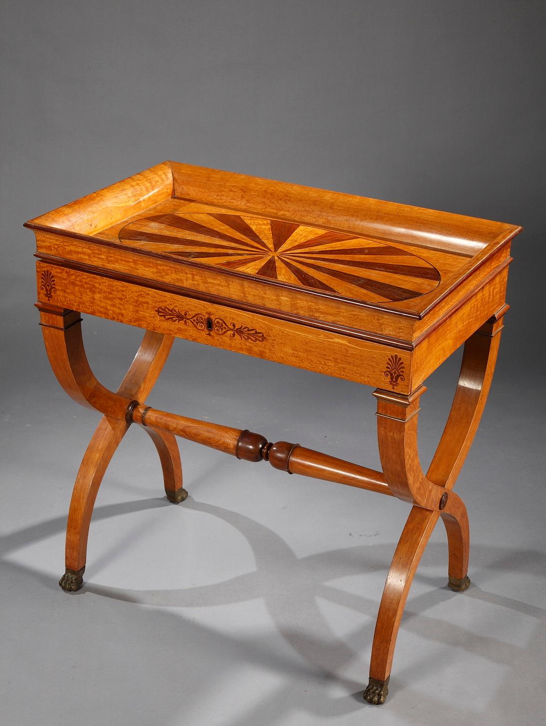 An elegant writing table from the Charles X period. The concave top is adorned with an ellipsoidal two-tone pattern. The belt, decorated with thin stylized ornaments, unveils a sliding writing surface covered with black and gold-tooled leather,