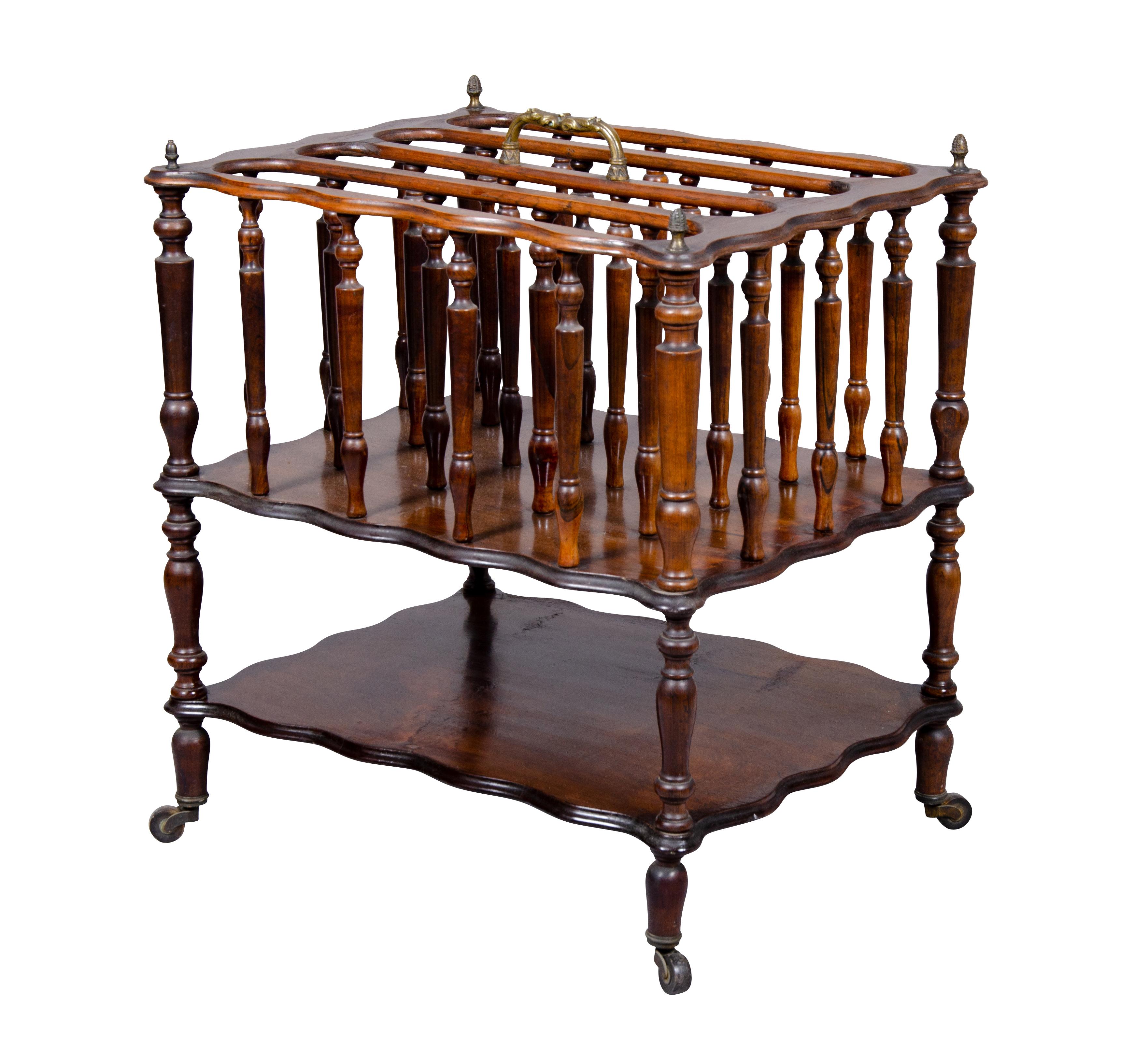 Constructed from solid rosewood. With brass carry handle over dividers with spindles , lower shelf, turned legs and casters. This form was designed by Hepplewhite for the Archbishop of Canterbury form holding sheet music and folios. Today its useful