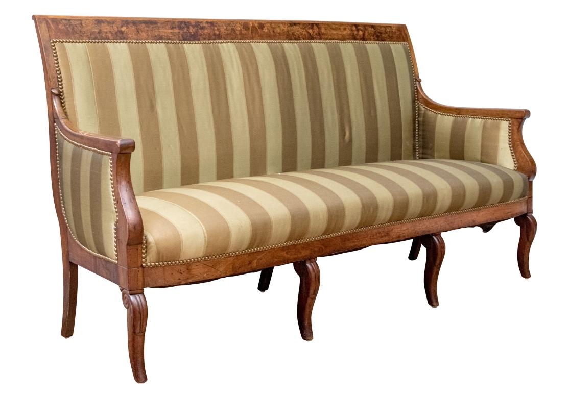 Ein Sofa im Charles-X-Stil mit Mahagonifurnieren, einer mit Wurzelholz furnierten oberen Schiene und gestreifter Polsterung mit Messingnägeln. Das Sofa ruht auf vier Kabriole-Vorderbeinen und drei säbelförmigen Hinterbeinen.

Abmessungen: 71 1/4