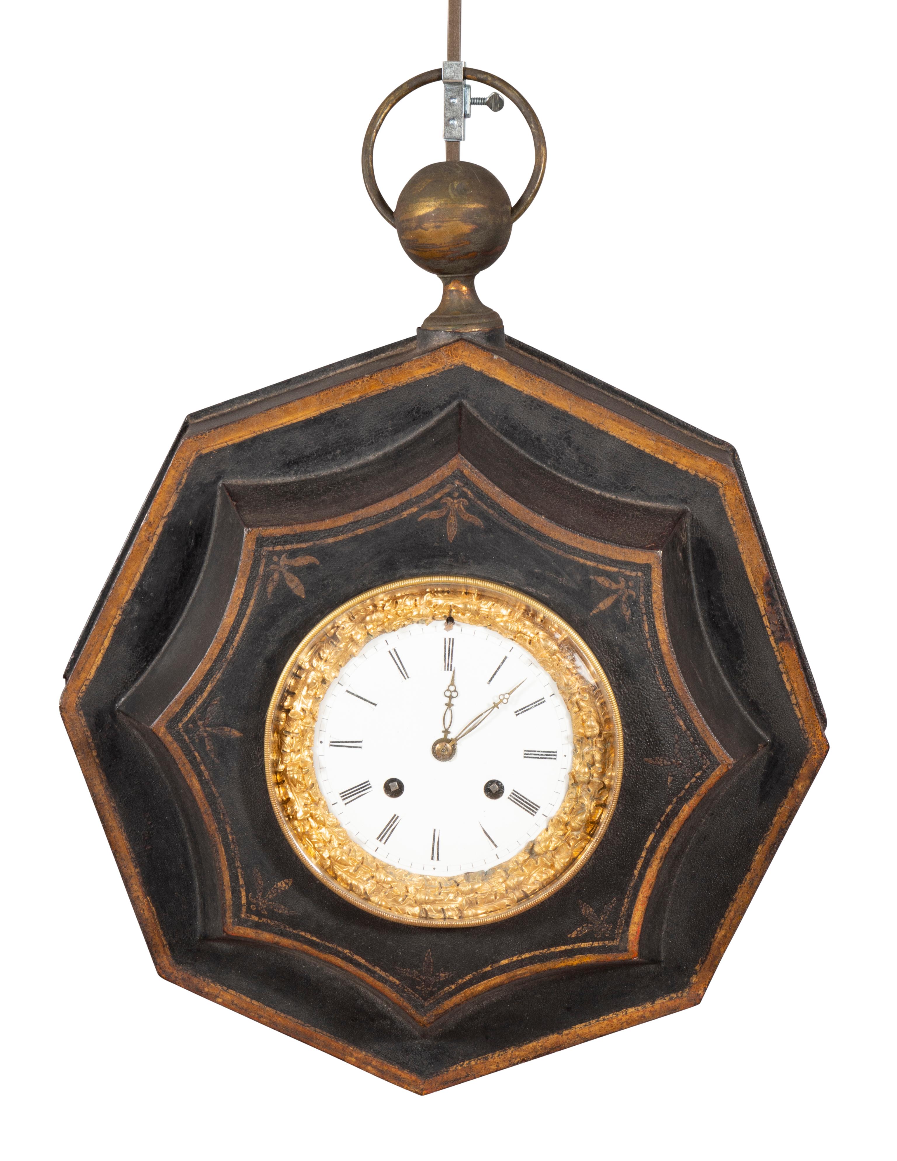 With a white enamel dial and gilt bronze bezel with its original works { currently unknown if it works }   Set in a black octagonal tole case with gilt details. Ring handle.