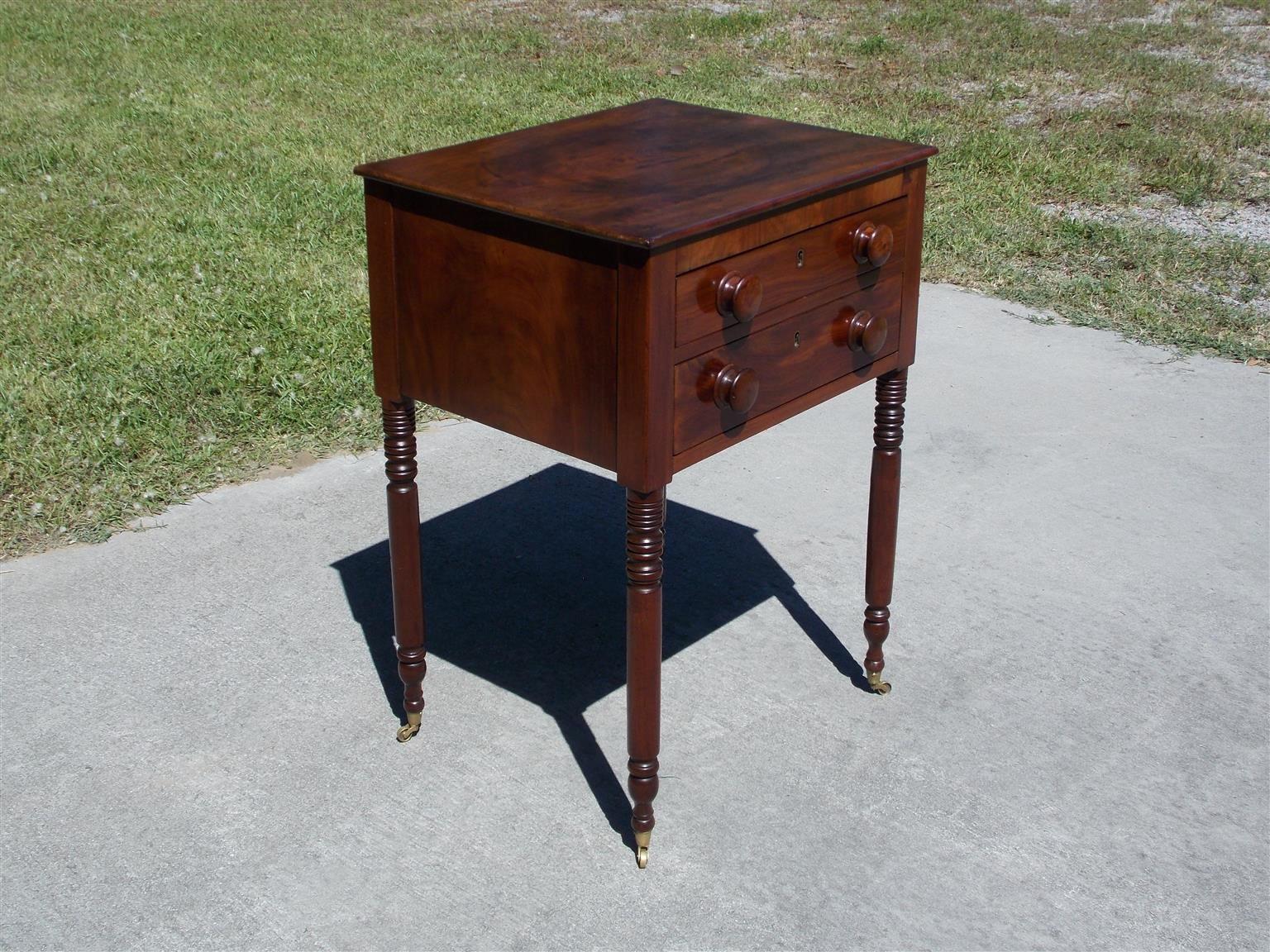 Charleston Federal mahogany two-drawer stand with a carved molded edge top, original wood knobs, and resting on turned bulbous ringed legs with the original brass cupped casters. Early 19th century. Secondary wood consist of poplar.