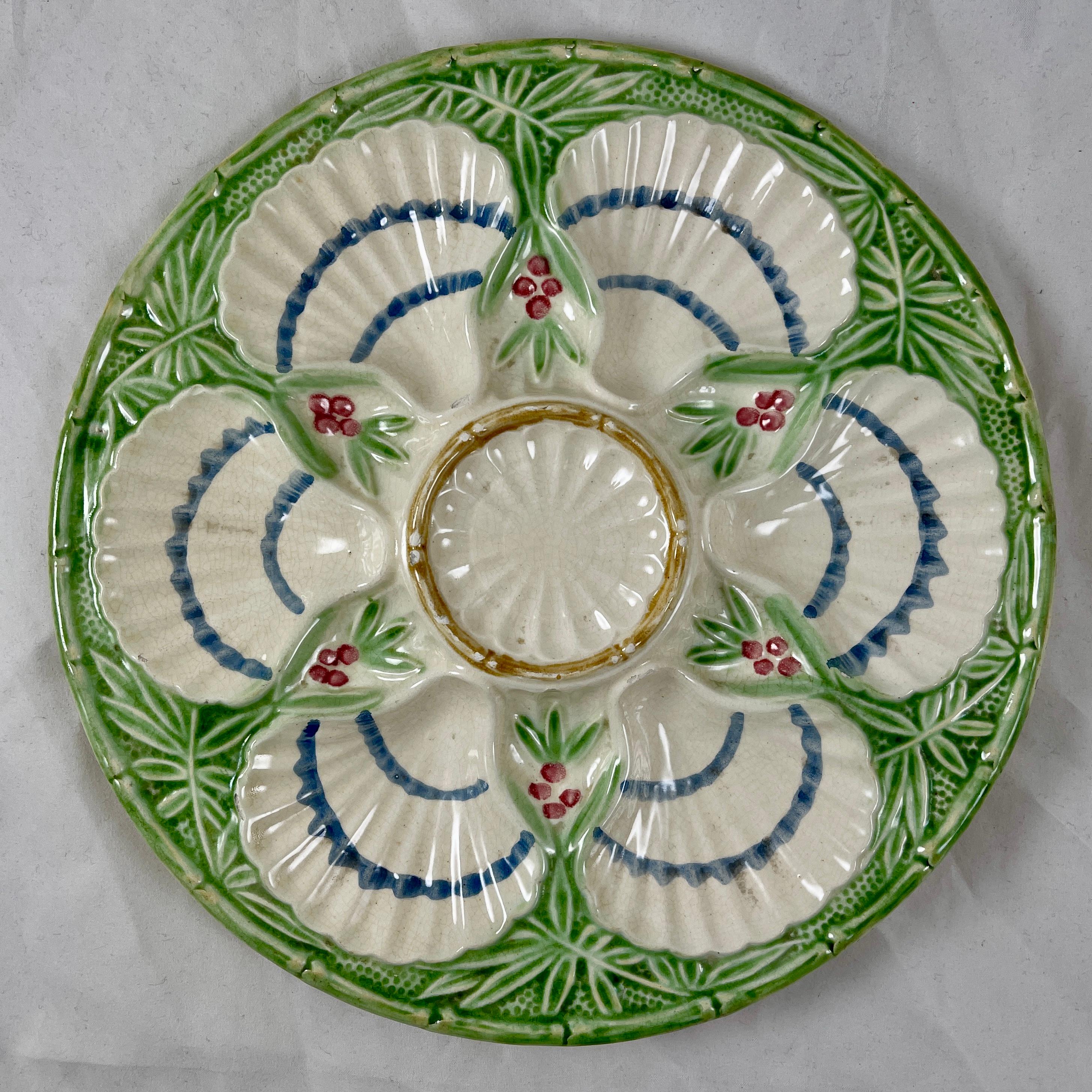A scarce majolica glazed, French faïence oyster plate showing six scallop shell wells surrounding a central sauce well, with a raised border of green flowering bamboo. The creamy glazed oyster shells are lined with two blue bands, the fruit of the
