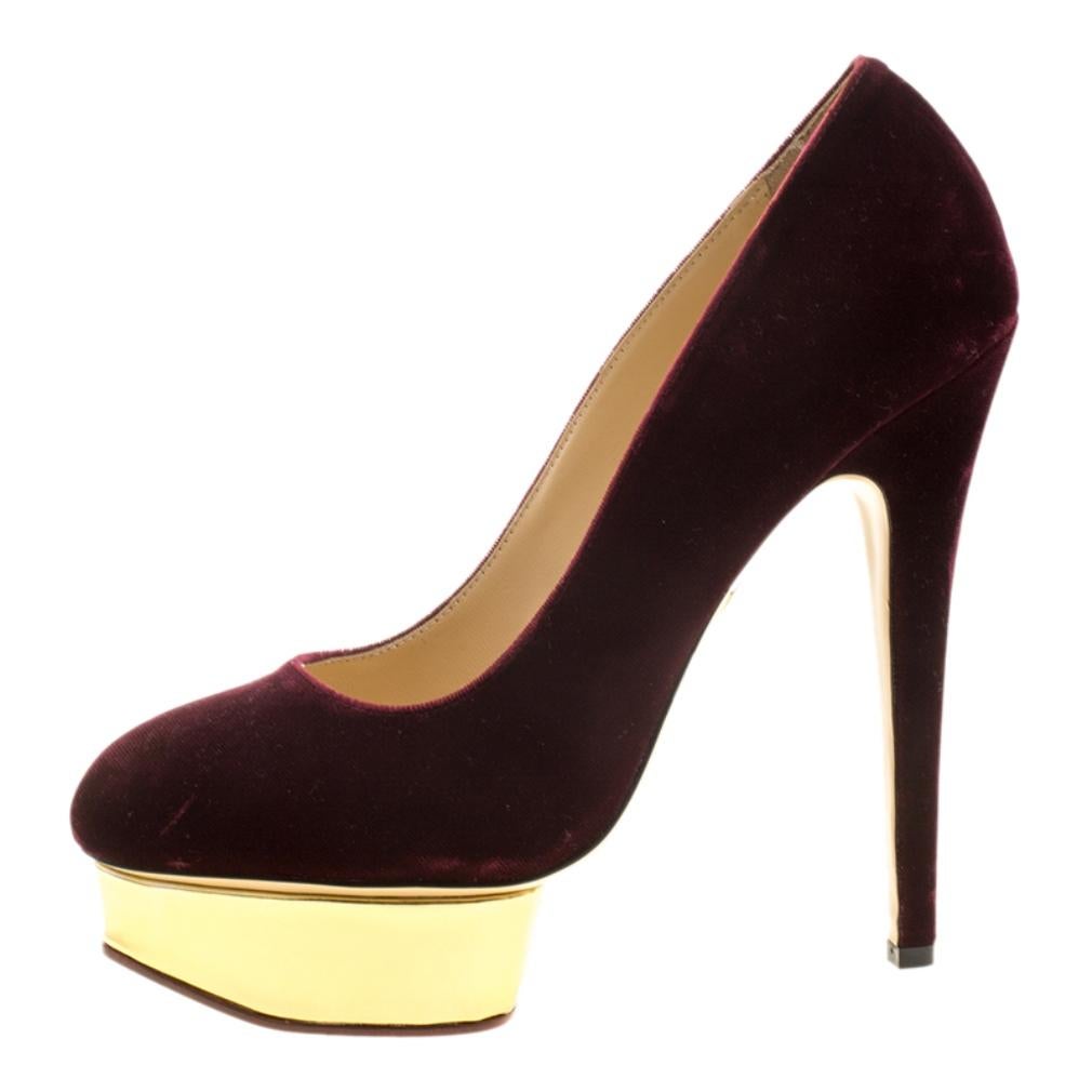 Charlotte Olympia's iconic Dolly pumps are a statement in themselves while completing your evening ensembles. Set on a gold-tone island platform, these pumps feature a stunning velvet body in a bold burgundy and rests on sleek heels. The perfect