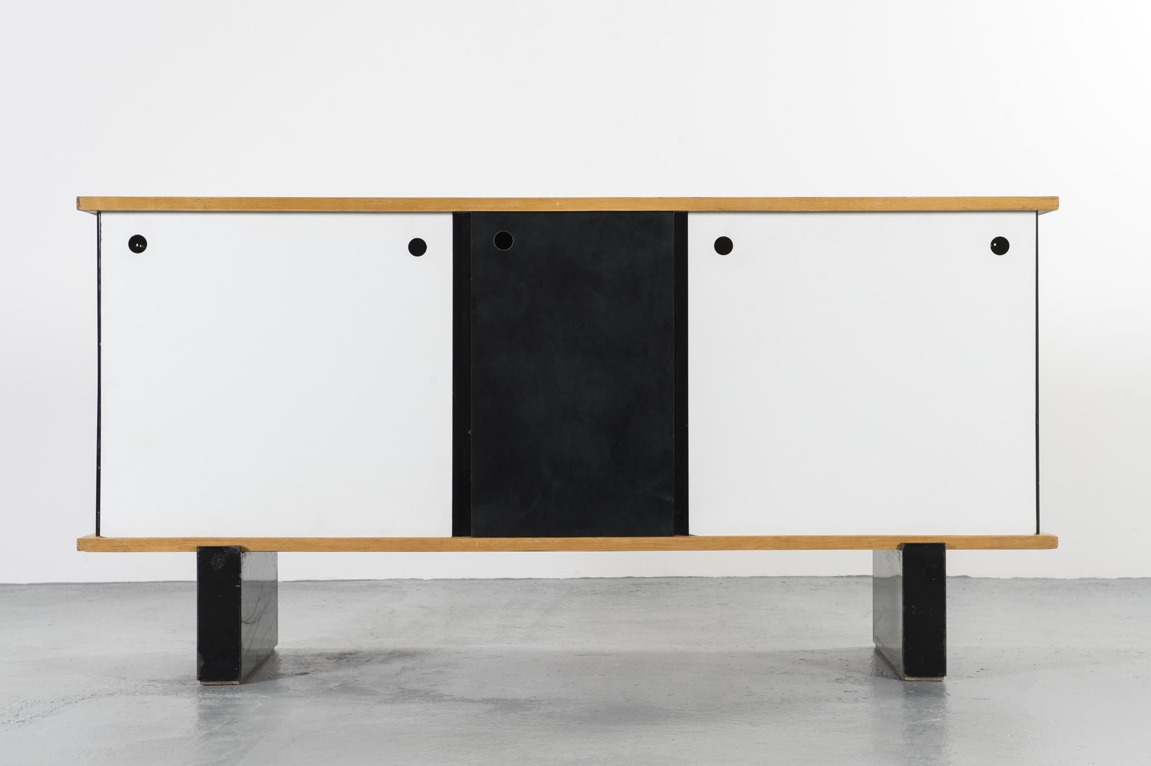 3-door sideboard designed by Charlotte Perriand for Cité Cansado, circa 1958
Edited by Galerie Steph Simon.

Top and inside shelves in ashwood, black lacquered base and feet in metal sheet, white melamine doors. 
The specificity of this sideboard is