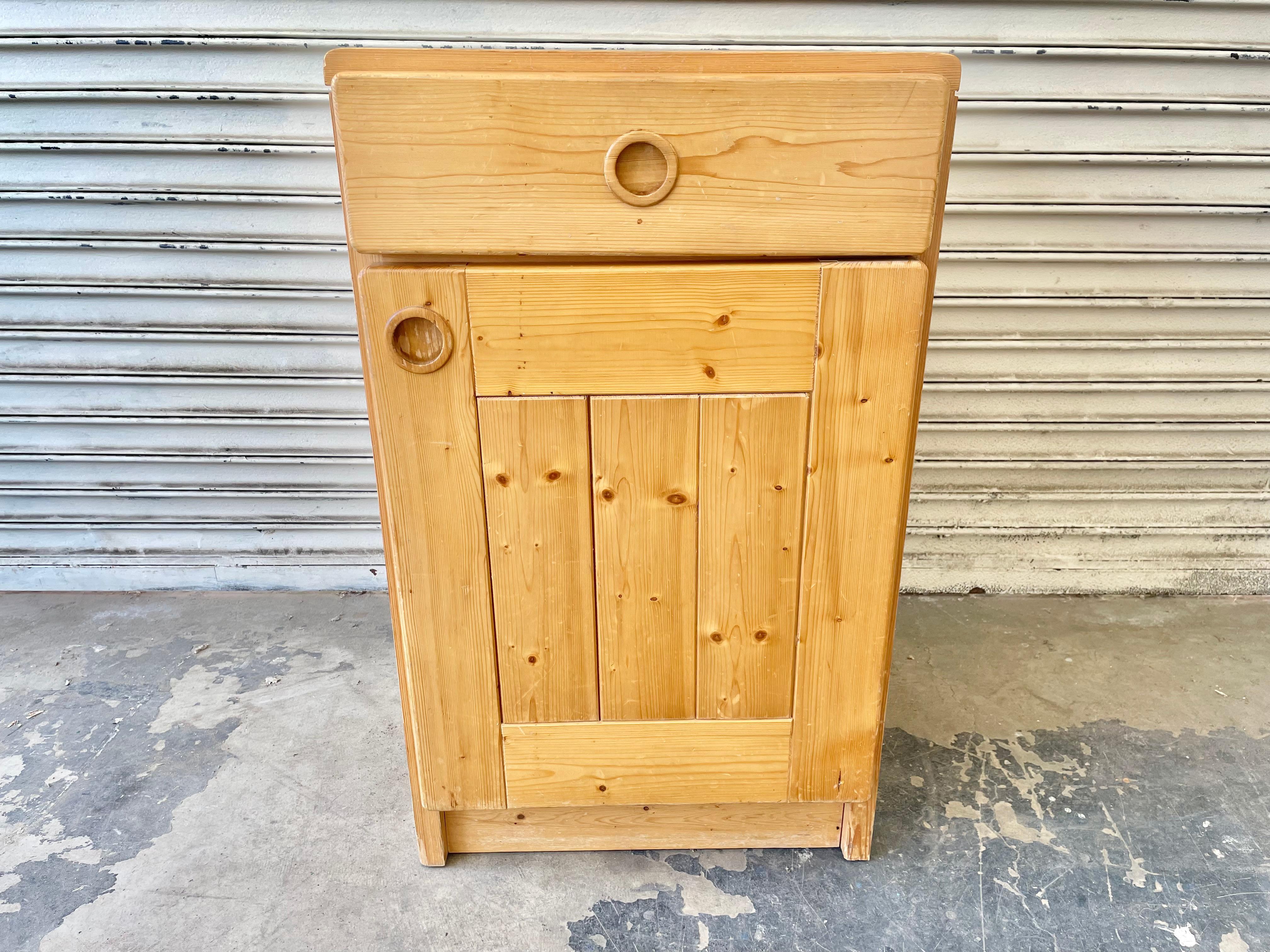 Pin bedside cupboard by Charlotte Perriand for Les Arcs. One pull out drawer. One door which opens to a shelf with two spaces for storage. Made of solid pine, circa 1960. Good original condition. Fun piece of collectible design from the popular