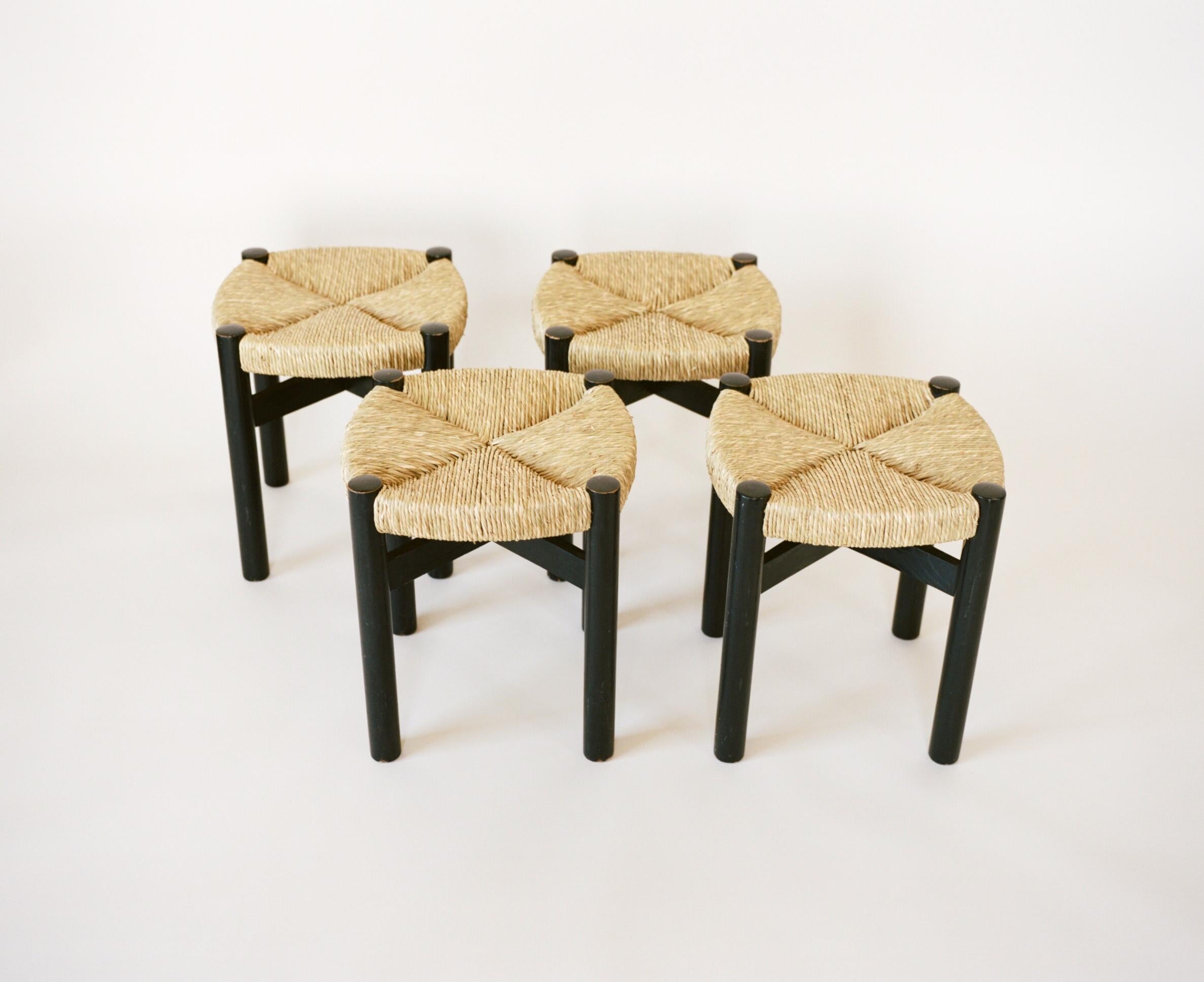 A set of four black oakwood stools with woven rush seats by Charlotte Perriand, circa 1950. Perriand produced these stools after her 6 year stay in Japan. Returning to Paris, Perriand was commissioned to design the interiors of Hôtel le Doron in