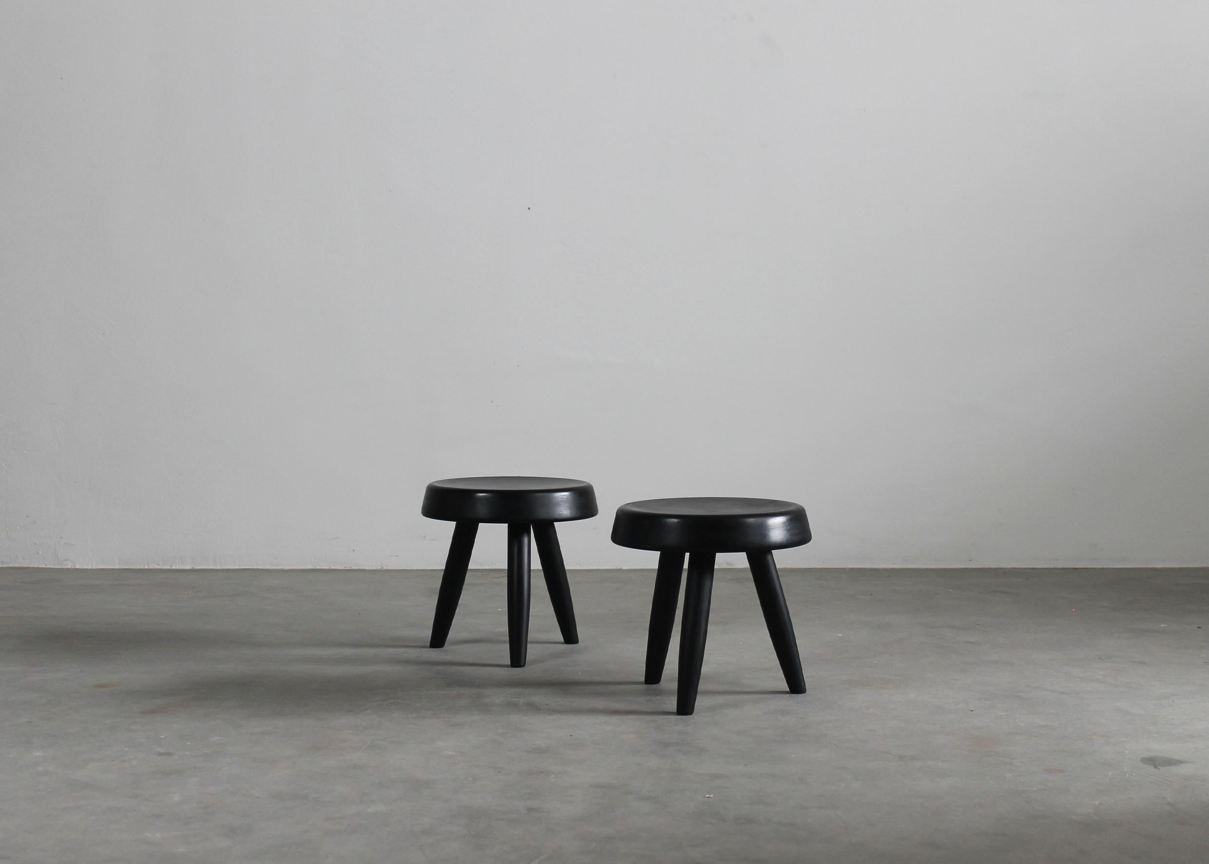 Set aus zwei Hockern mit drei Beinen, komplett aus schwarz gebeiztem Holz, entworfen im Stil von Charlotte Perriand und hergestellt in den 1950er Jahren. 

Charlotte Perriand (1903-1999) ist eine der bedeutendsten Möbeldesignerinnen der Mitte des