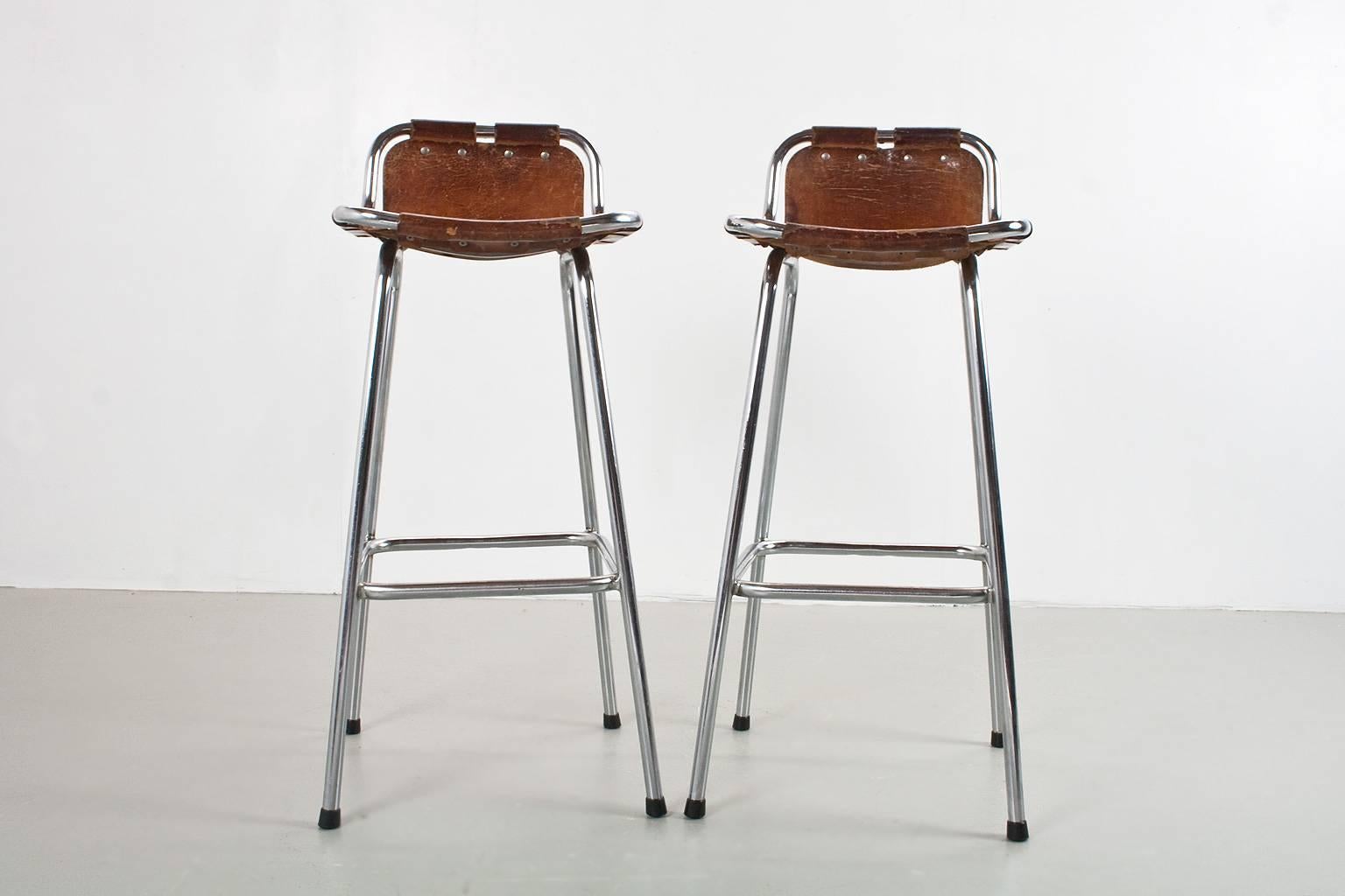An original pair of midcentury modern French lightweight high bar stools with brown camel colored saddle leather sling seats, on a chromed tubular frame selected by Charlotte Perriand for the “Les Arcs” ski resort in France, 1960s. The chromed frame