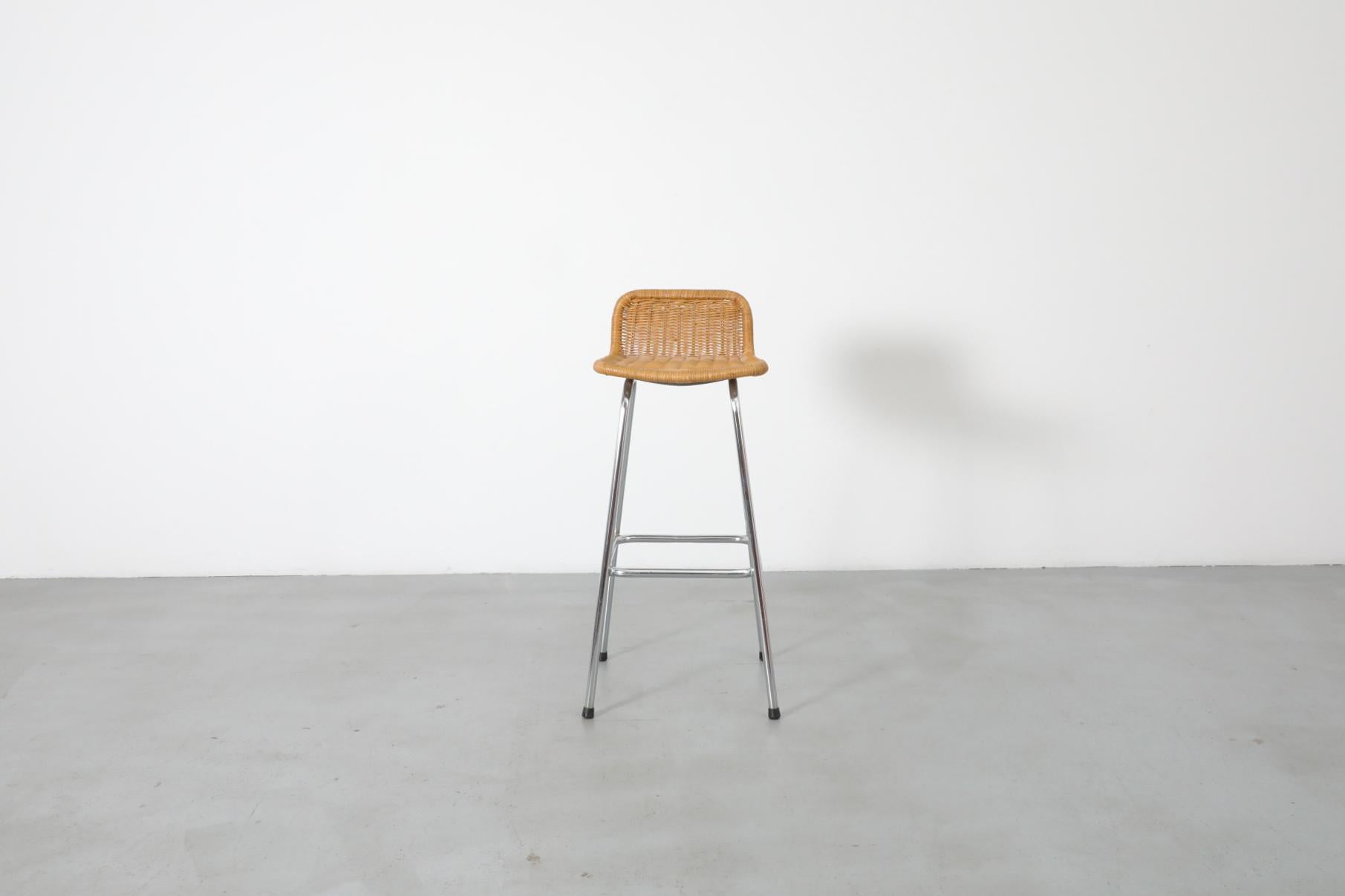 Taburete de bar estilo Charlotte Perriand con respaldo bajo redondeado de ratán y estructura tubular cromada. En estado original, con desgaste visible propio de la edad y el uso. La altura total es de 34,25