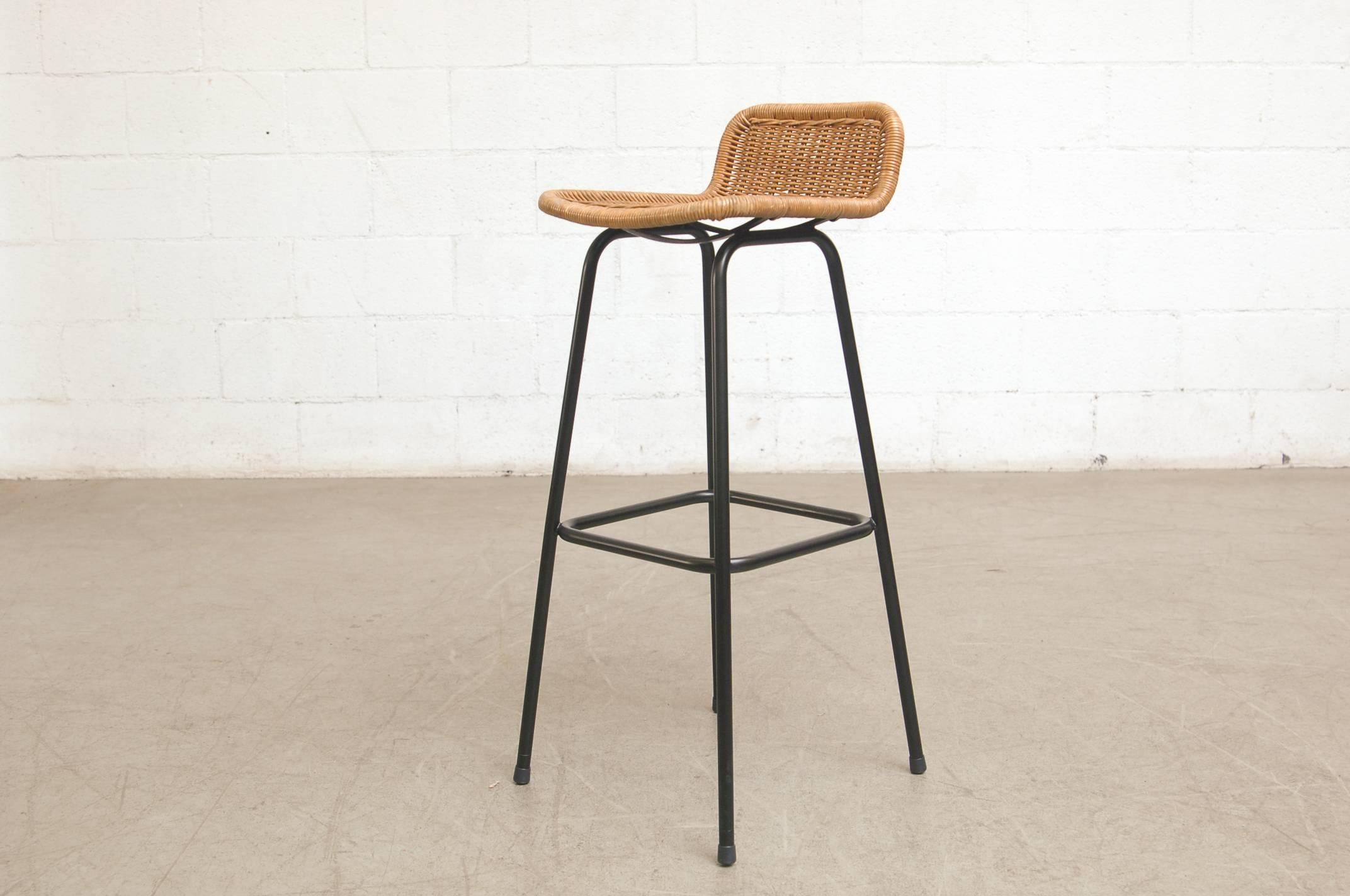Charlotte Perriand style low rounded wicker back bar stools with black enameled tubular frames. Visible wear to rattan, minimal losses. Wicker colors vary from stool to stool, as well as wear to seats and frames. In original condition with visible