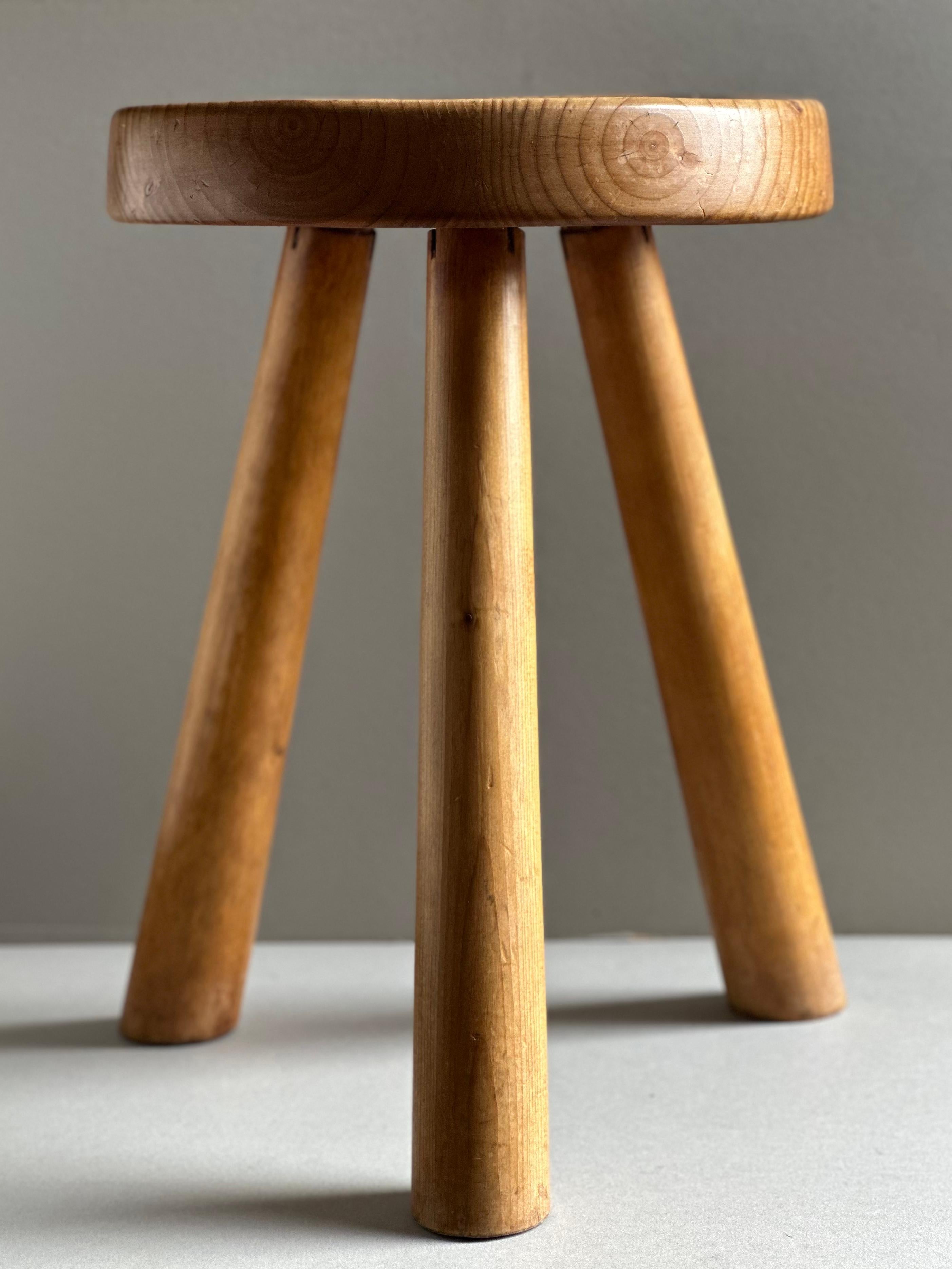 Tripod stool in pine designed by Charlotte Perriand for Les Arcs Ski Resort in Savoie, France, comprising a concave seat supported by tapering dowel legs. All original condition with an even, untouched patina.