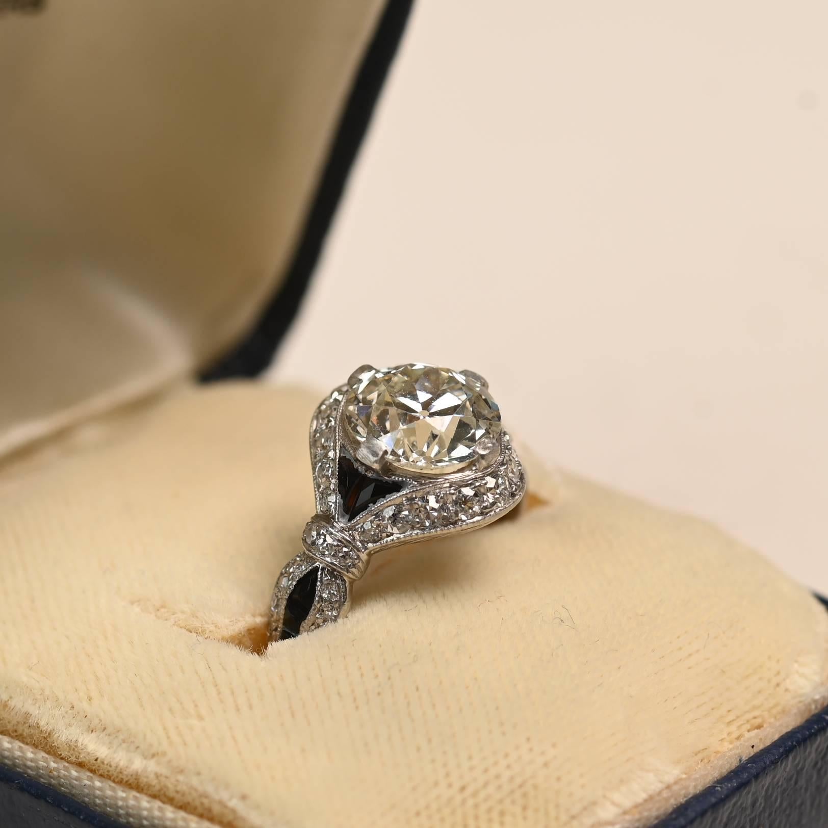 Un extraordinario anillo Charlton de la época Art Decó que exhibe un diamante de talla europea antigua de aproximadamente 2,10 quilates de color K y claridad VS1. La piedra central está enmarcada en un distintivo diseño geométrico engastado con