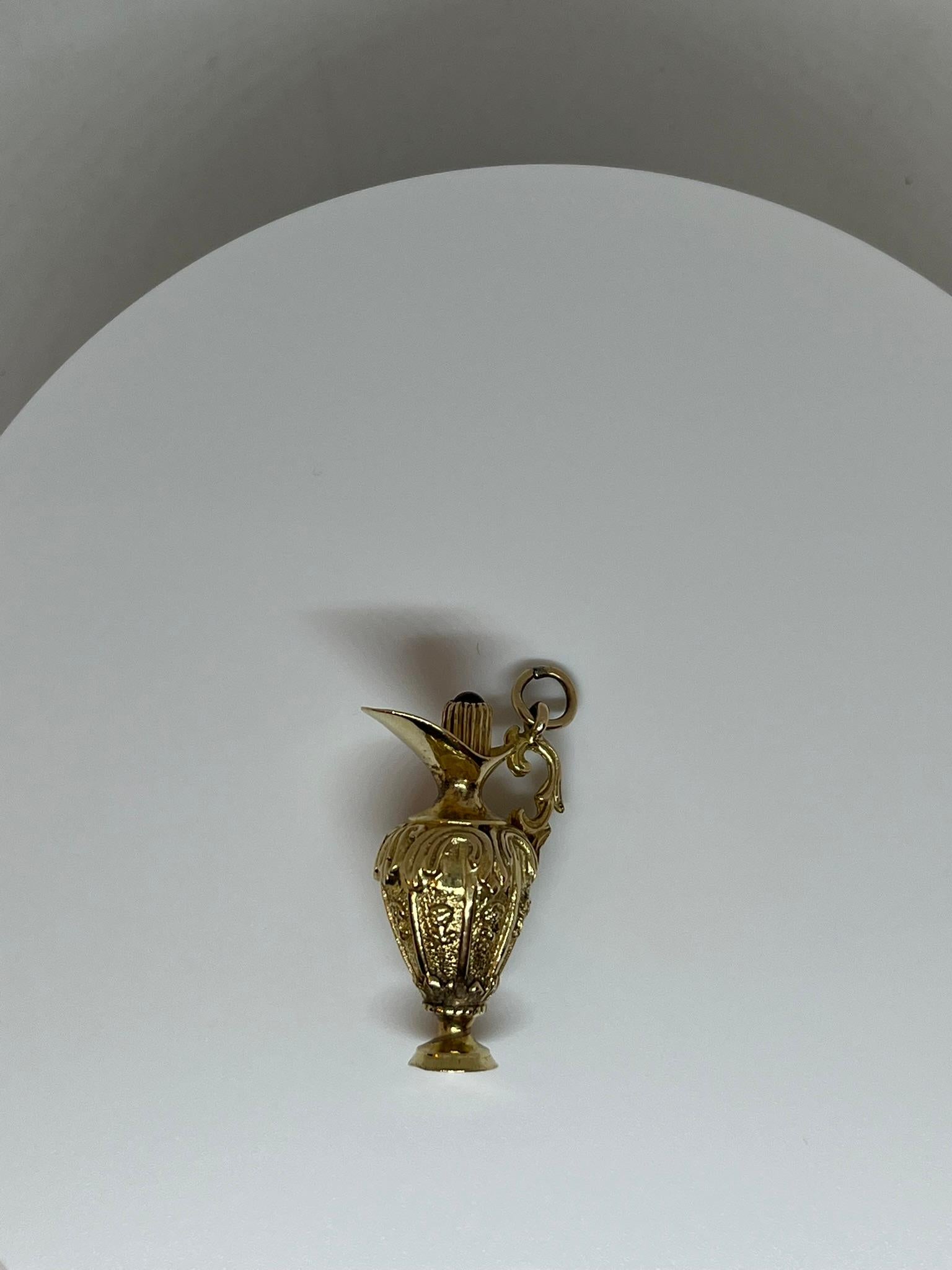 Dieser Vintage-Anhänger aus 18 kt. Gold in Form einer Amphore ist reich mit Reliefs verziert, unter denen sich florale Motive abzeichnen. Am Henkel der Amphore ist ein Ring angelötet, mit dem sie an einer Kette oder einem Armband befestigt werden