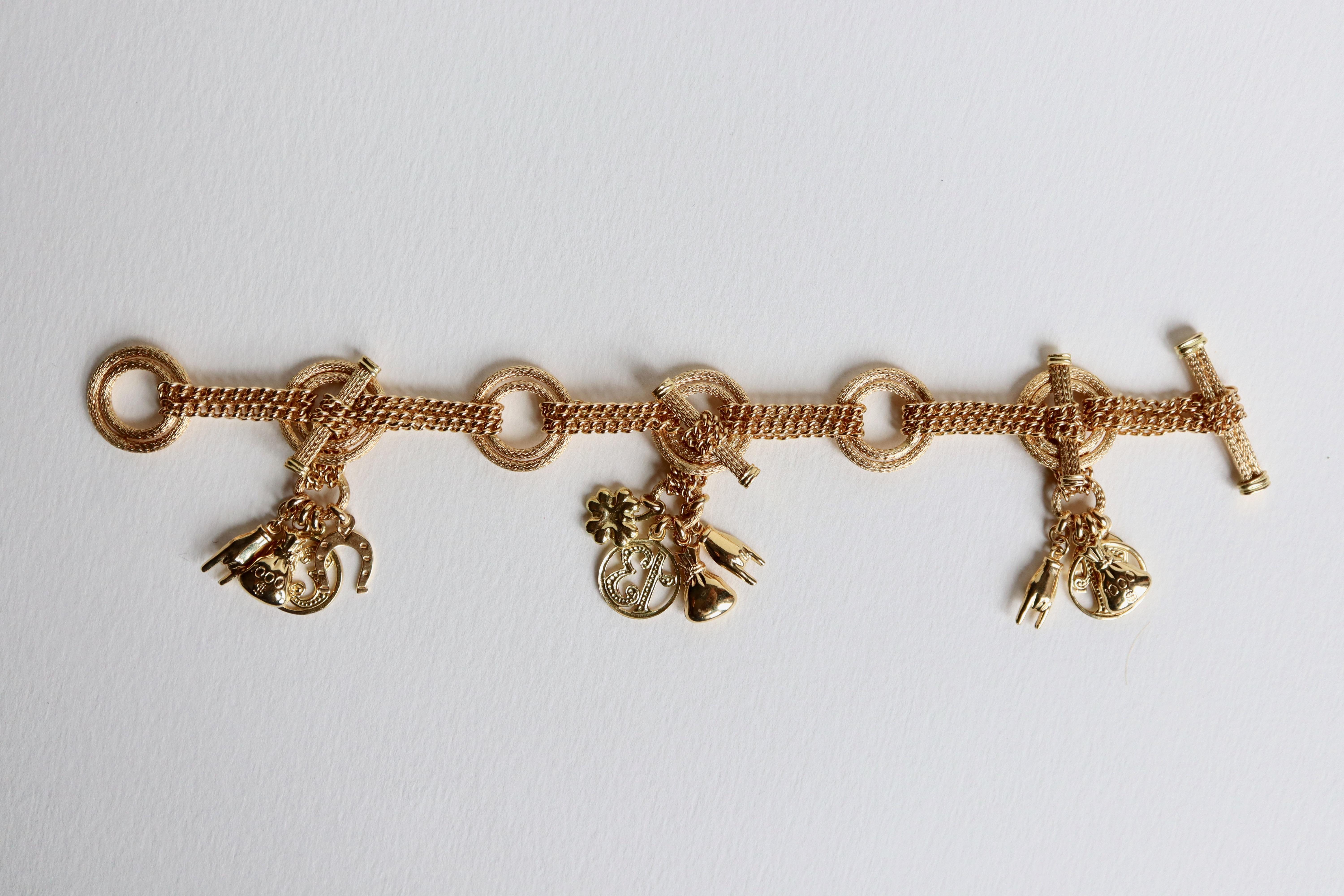 Charms bracelet in 18 carat yellow gold Double chain alternating with double chiseled circles retaining 3 groups of detachable charms, on each group: a number 13, a hand, a bag of 1000 dollars, a horseshoe and a clover with 4 leaves. Stick clasp.
