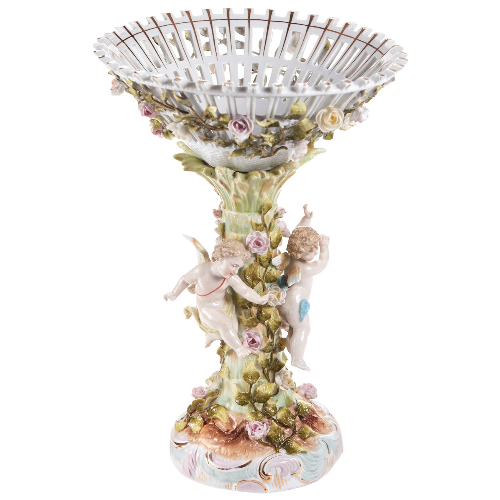A charming 19th century Meissen style pedestal comport. The openwork bowl applied with delightful trailing flowering vinery and supported on a column applied with three pretty winged putto and conforming rose vinery.
       