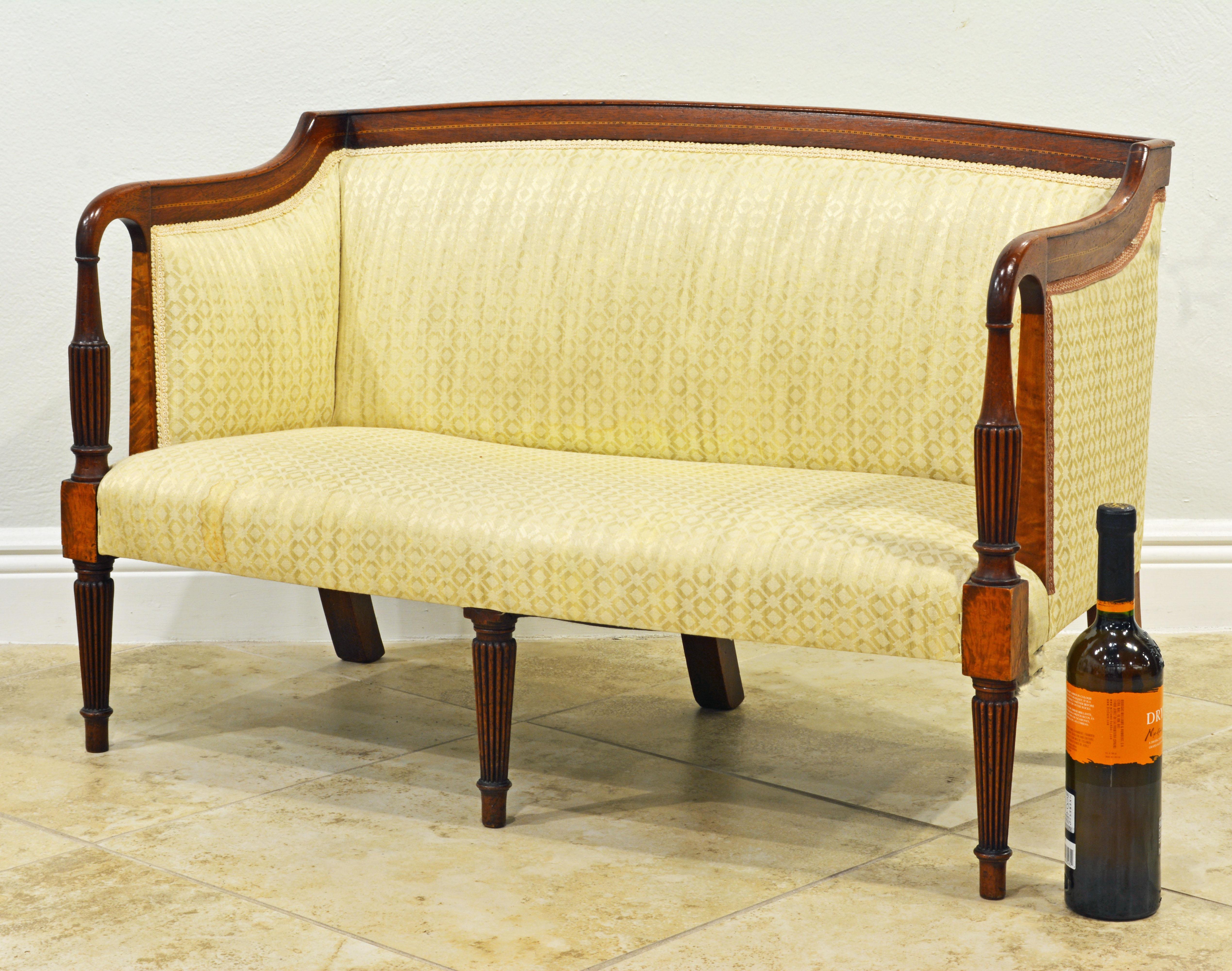 This charming diminutive English Sheraton style mahogany children's settee features a slightly arched and inlaid back and side rail continuing to the armrests terminating in bulbous reeded supports flowing into a block at the seat supported by three