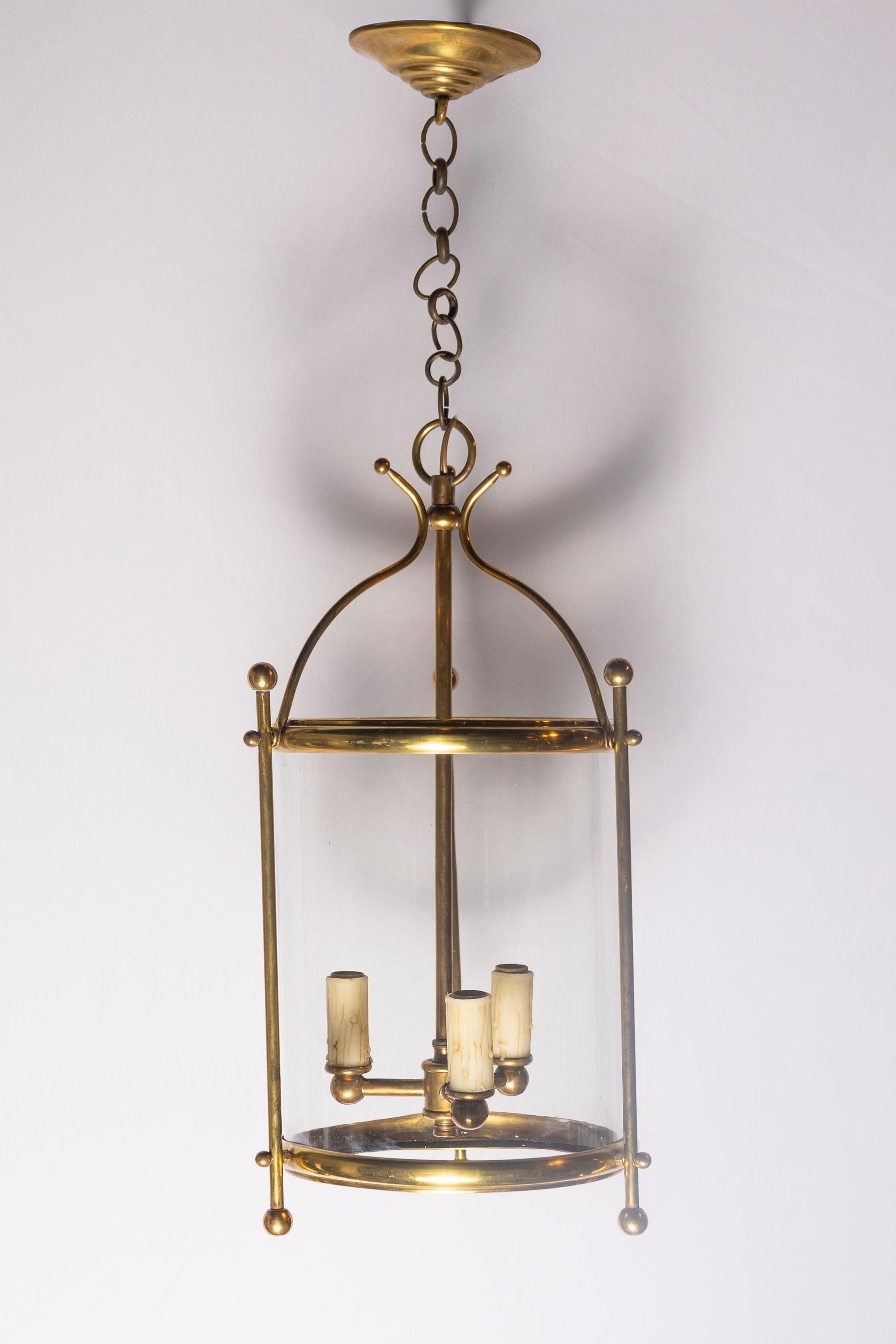 Cette élégante lanterne française du début du XXe siècle est dotée d'un cadre en laiton aux lignes épurées et d'un design minimaliste et raffiné qui s'intègre aussi bien dans les intérieurs classiques que contemporains. La structure cylindrique est