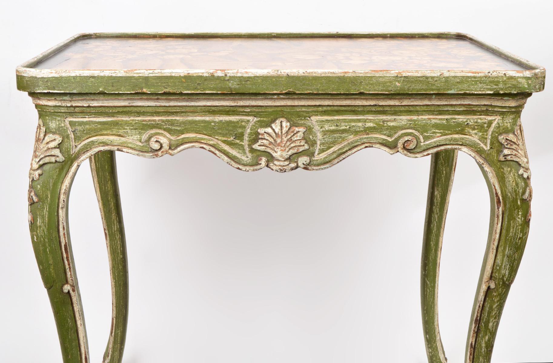 Dating to the mid 20th century this charming table in the Louis XV style features a top painted with flowers on a table cloth above a shaped, carved and decorated frame resting on four likewise carved and decorated cabriole legs. Paint and gilt