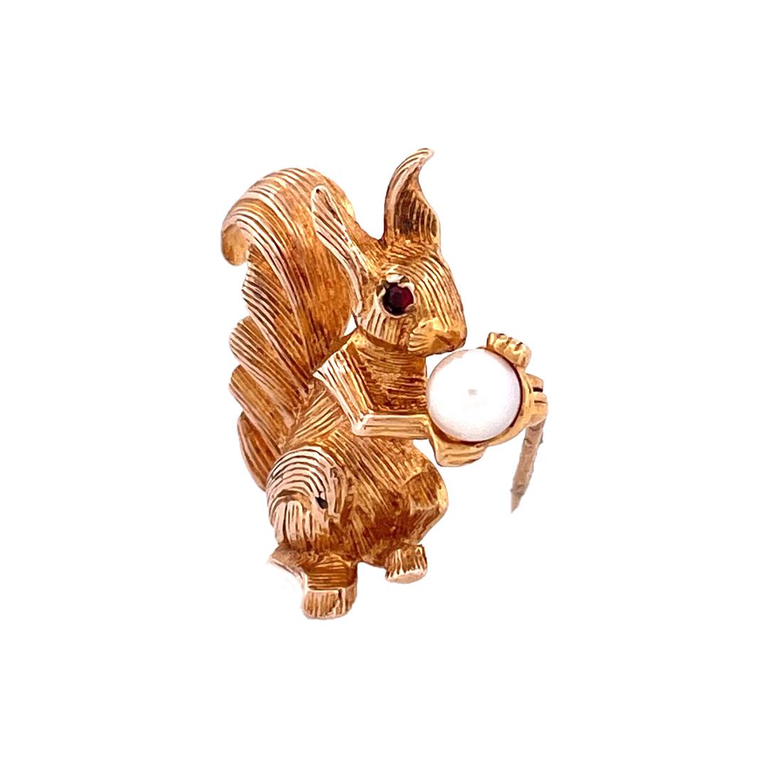 Embrace the whimsical allure of our 9K yellow gold Squirrel Brooch. This delightful piece features a squirrel in a sitting pose, where squirrel's eyes are adorned with ruby gemstones, and the squirrel holds a lustrous pearl in its tiny hand. Crafted