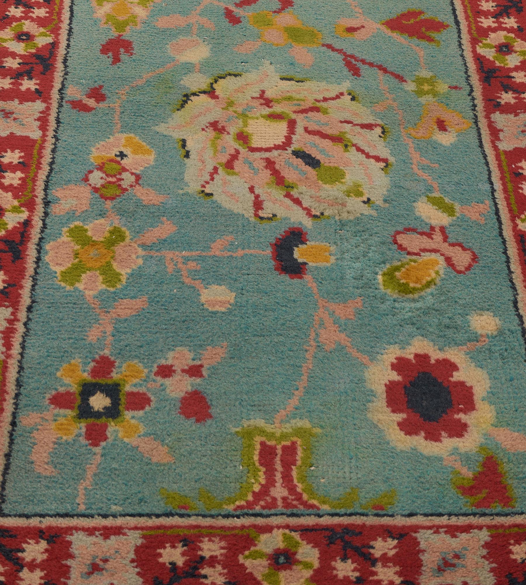 This antique Irish Donegal runner has a shaded turquoise field with a dusty-pink, tomato-red, lime-green scrolling flowerhead and leafy vine around a column of four bold similarly colored palmettes, in a narrow tomato-red border of dense flowerhead