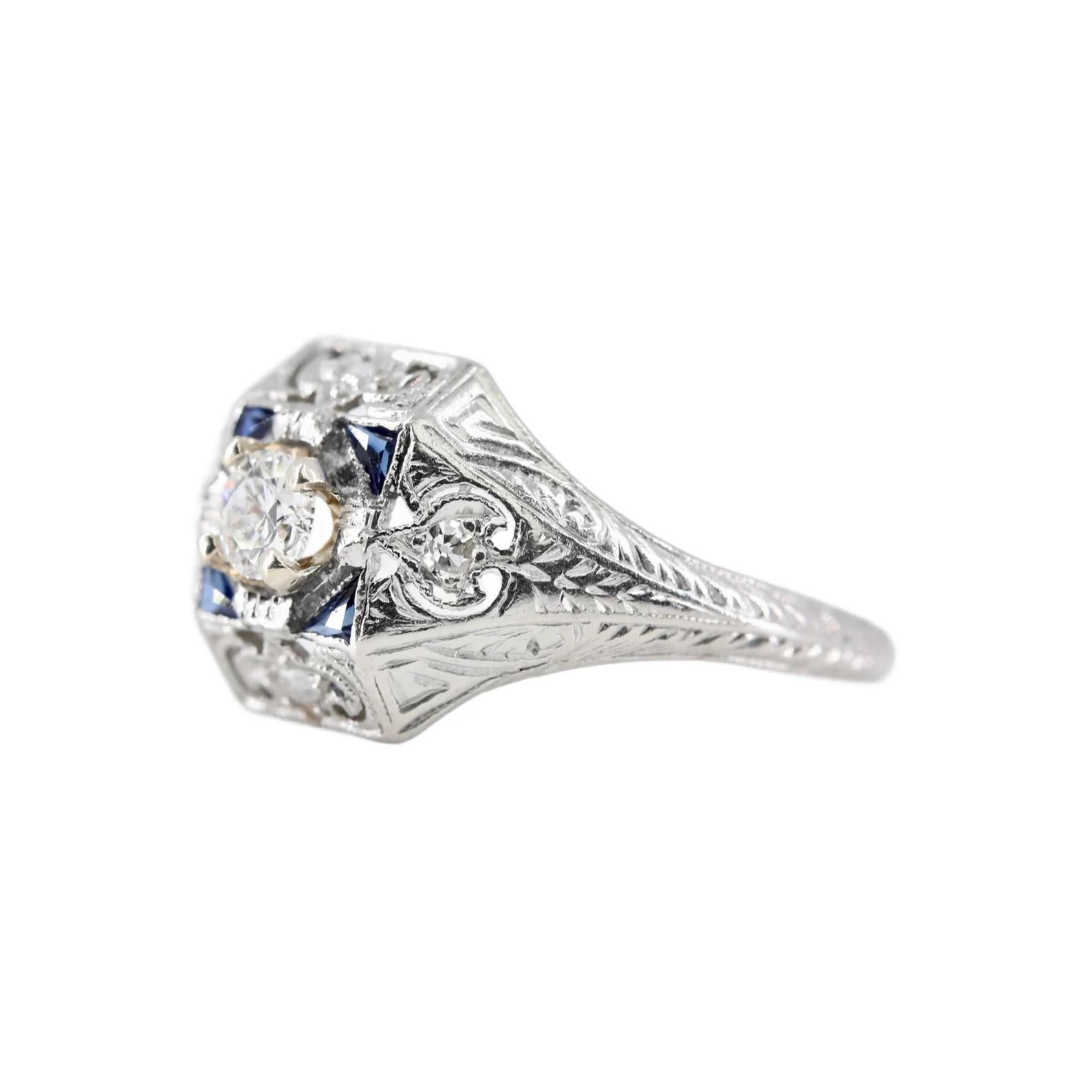 An art deco period diamond, and sapphire engagement ring in platinum. Centered by a 0.25 carat round cut diamond of H color, VS clarity. Accenting this ring are four additional diamonds of 0.04ctw, and four French cut sapphires. Completed by hand