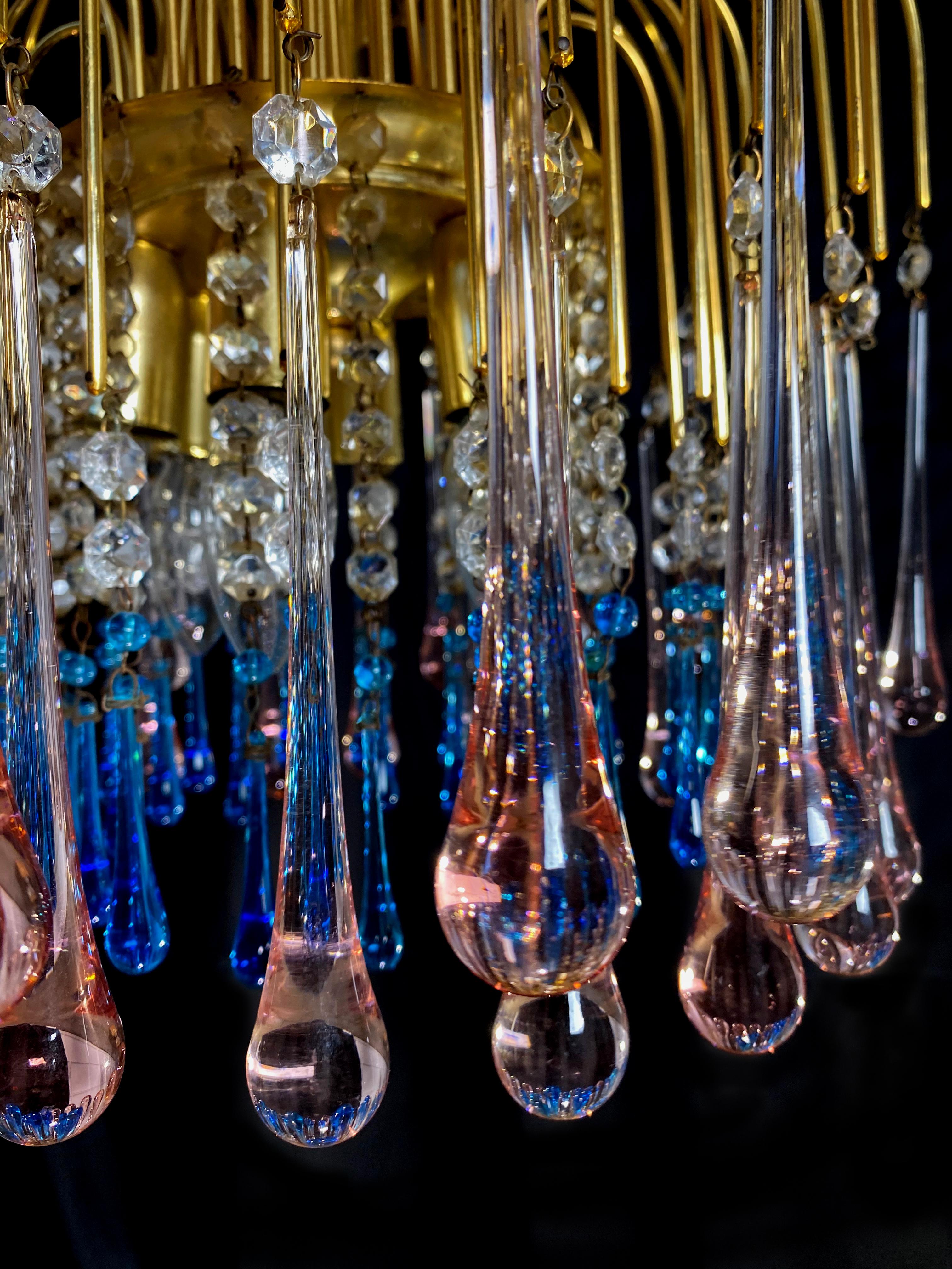 Elegant Venetian chandelier. Dozens of blue and pink drops hang from the golden canopy. Five small lights.
  
