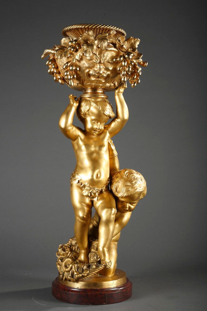 Signed Cumberworth and Susse Fres

A charming gilded bronze group representing two children with a basket of flowers at their feet and holding up a large vase ornated with a lion skin, vine branches and grapes. Reposing on a moulded red griotte