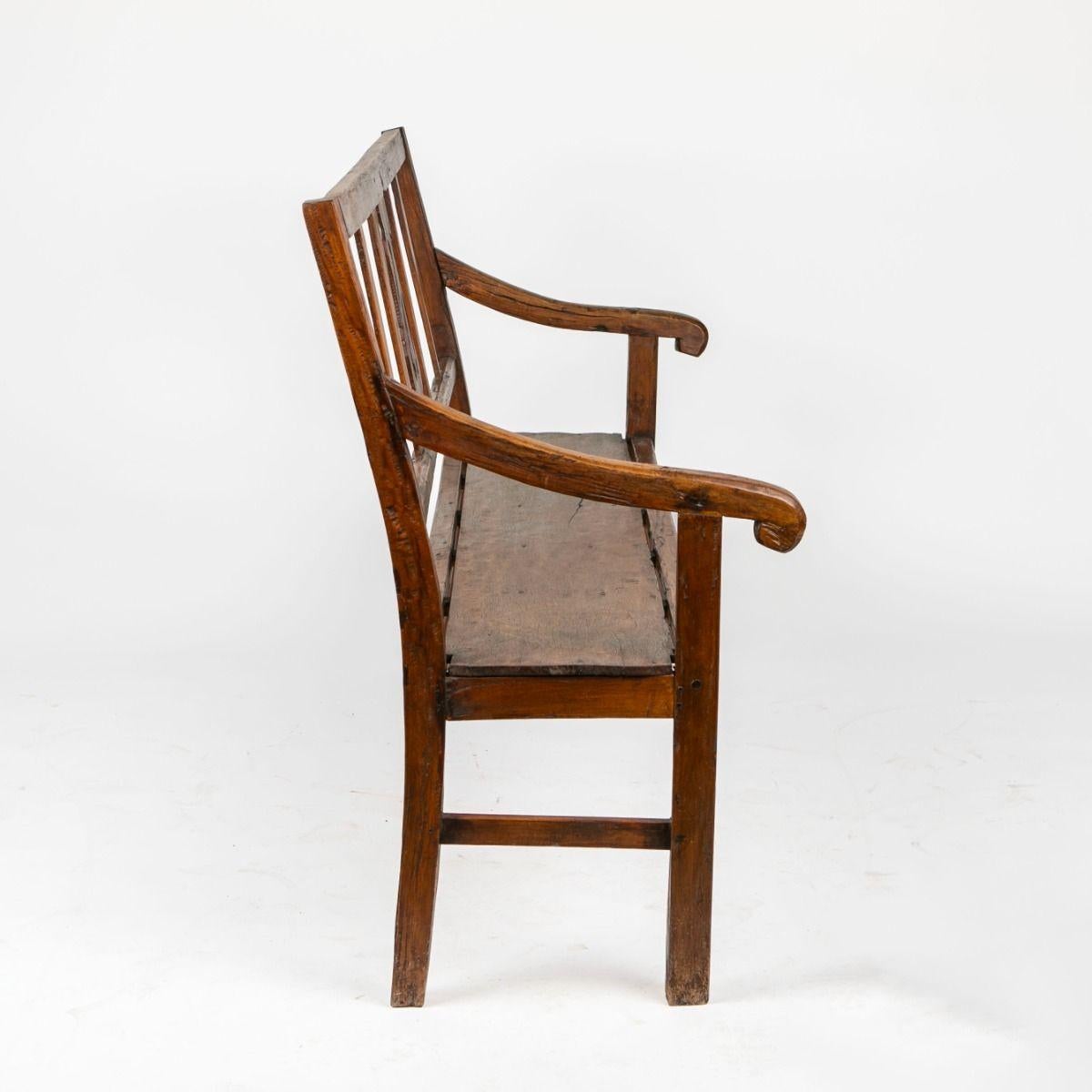 A charming bench crafted from solid narra hardwood, featuring a natural patina that reflects its age and use. The backrest is adorned with a simple yet decorative central carving, inspired by the classical forms of the Empire style. The subtly