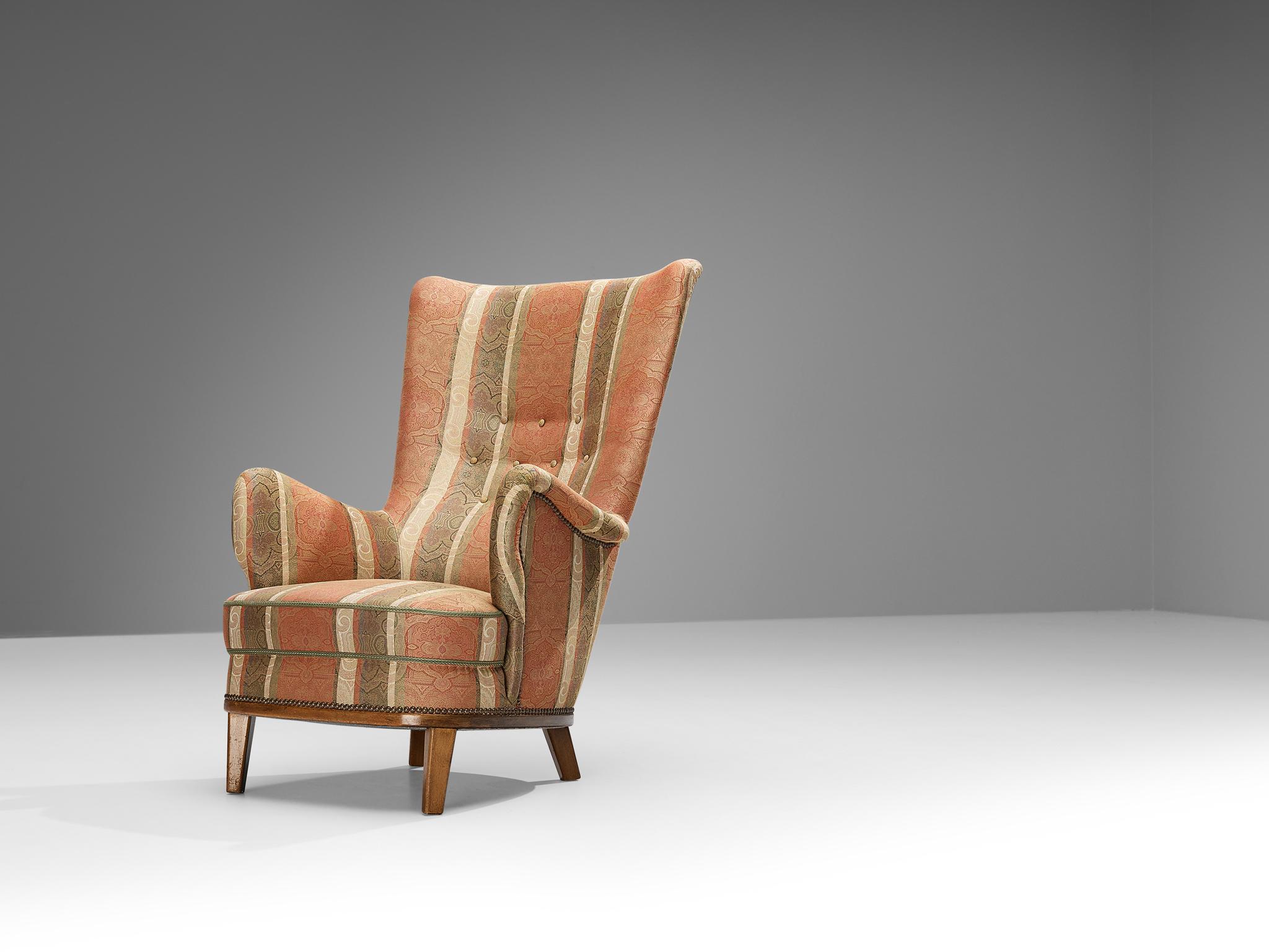 Lounge chair, fabric, brass, beech, Denmark, 1950s

This wingback armchair of the 1950s is both visually appealing and exceptionally comfortable. Its striped fabric features a blend of pink-orange, brown, and beige strokes, accentuated by green