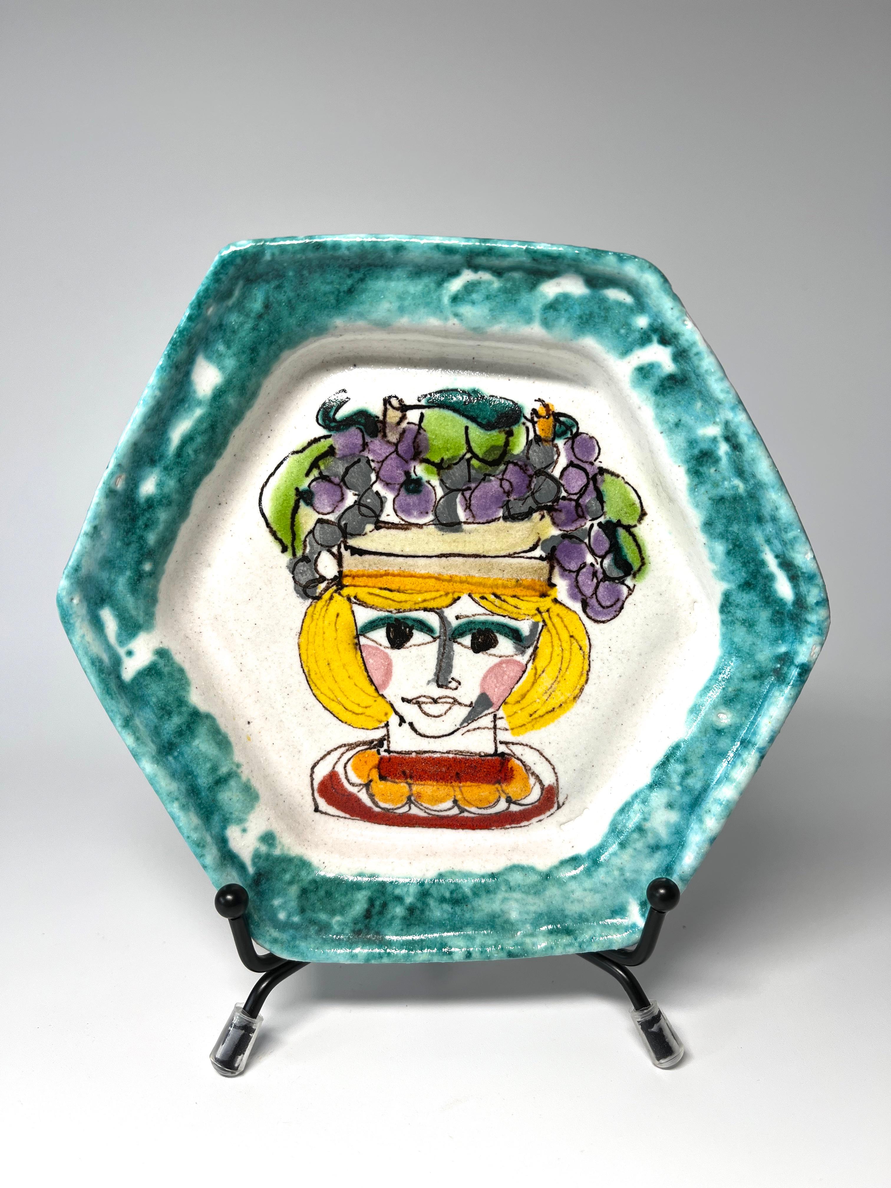 Ravissante petite assiette hexagonale en céramique de DeSimone (Italie)
Décorée à la main d'une femme coiffée d'un chapeau de raisin et bordée d'un bord pointillé vert d'eau.
Circa 1960's
Signé DeSimone, Italie
Hauteur 0,75 pouce, Diamètre 5,5