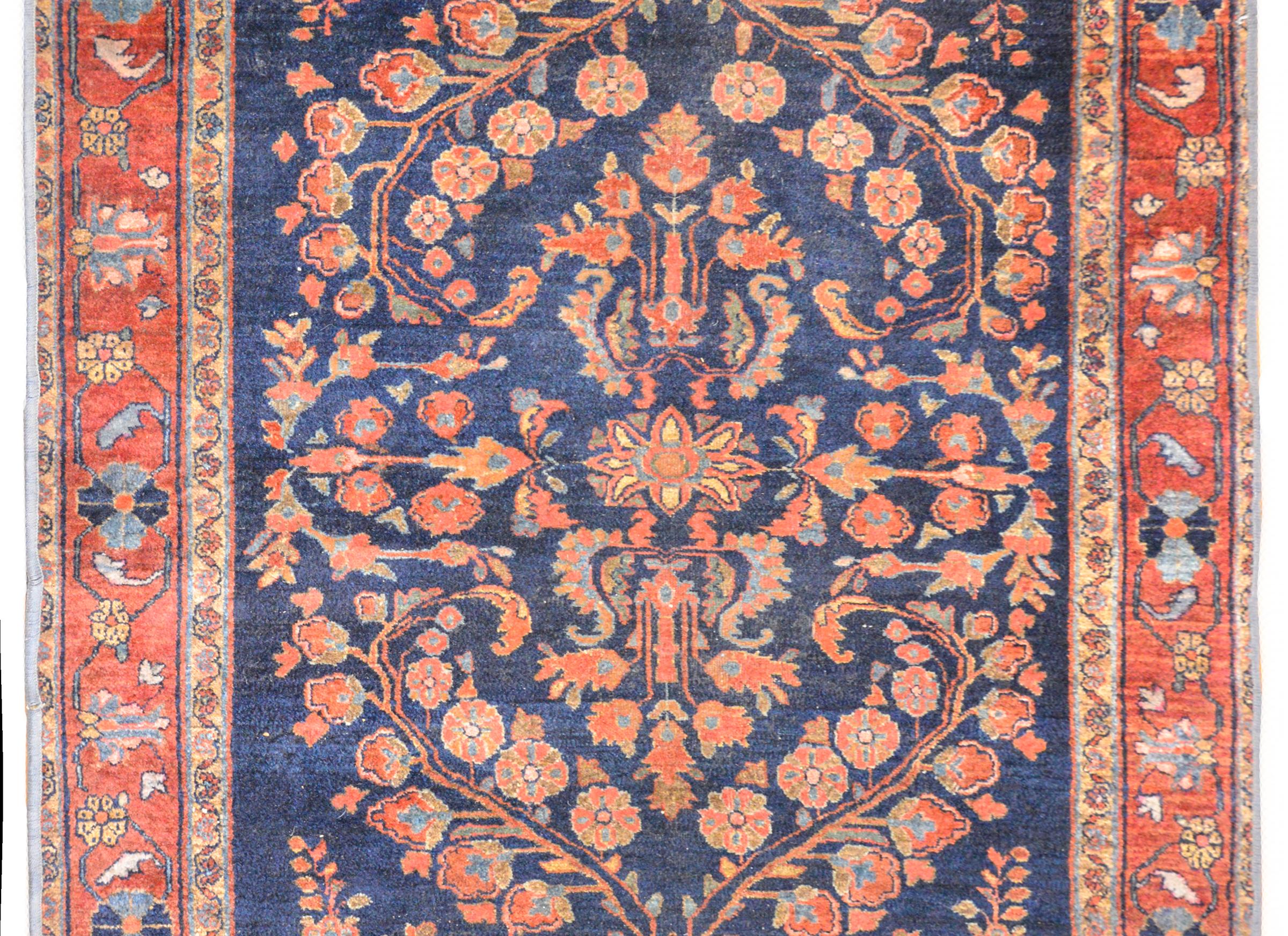 A charming early 20th century Persian Sarouk rug with a beautiful mirrored scrolling vine and floral pattern woven in coral, orange, pink, and indigo against a dark indigo background. The border is wonderful with a beautiful floral and scrolling