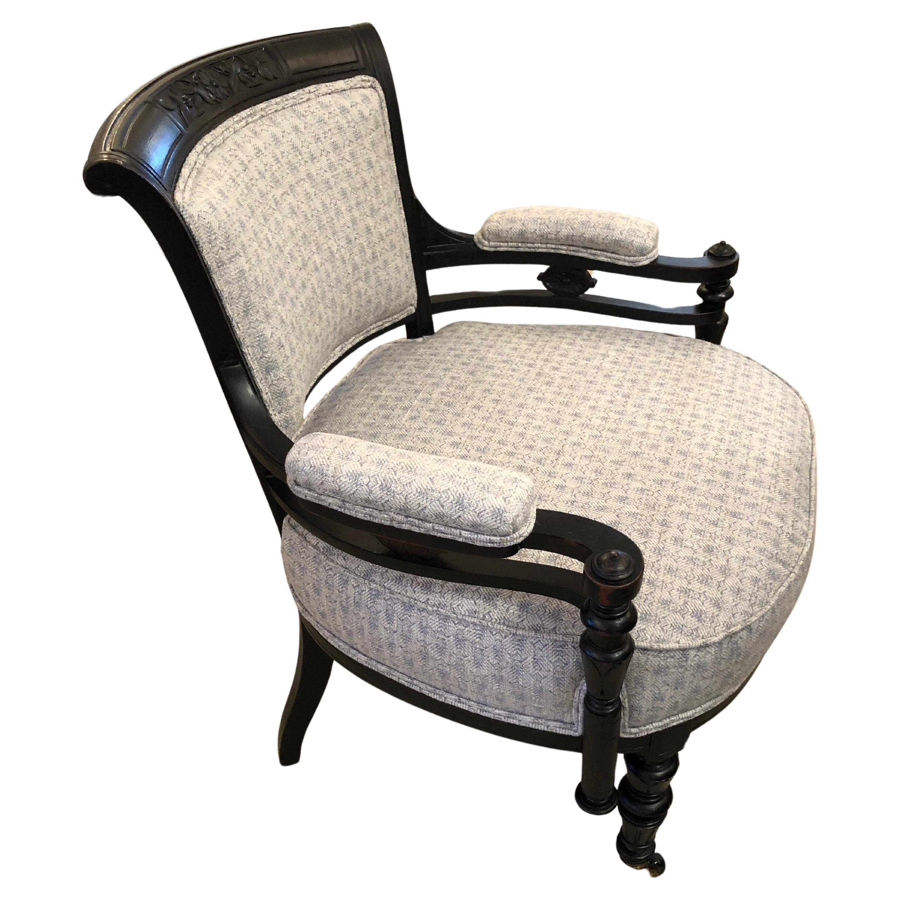 Charming compact curvy ebonized carved wood armchair in decorative Victorian style having flowers carved into the top and fancy turned wood details.  The chair has been beautifully updated and glamorized with new light bluish grey upholstery.  The