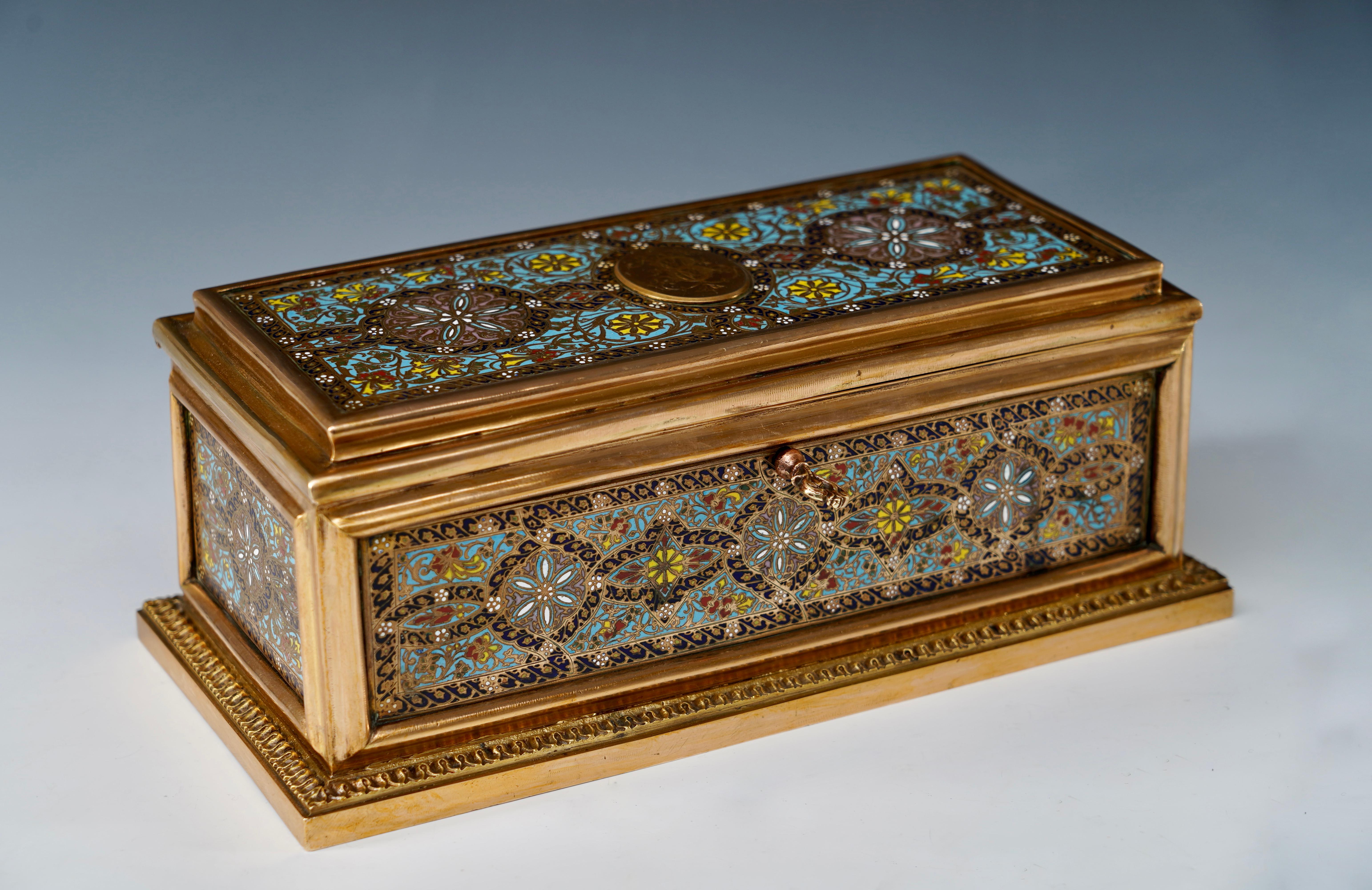 Signed Tahan, Boult des Italiens 11

A lovely rectangular casket made in gilded bronze, entirely decorated with polychrome “champlevé” enamel rosettes and stylized flowers, and embellished on the top with a monogram. It has preserved its original