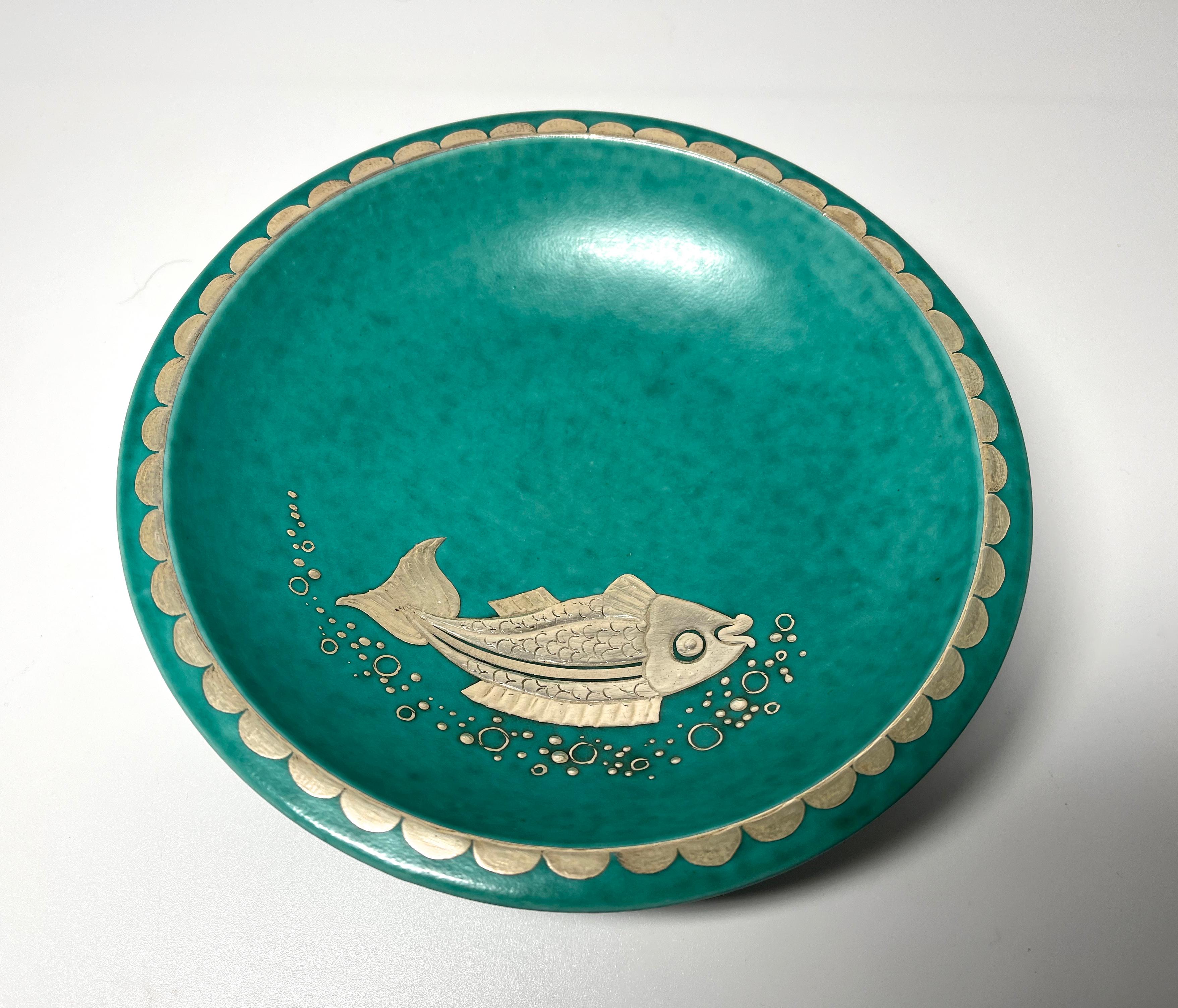 An expressive silver fish adorns this elegant footed dish by Wilhelm Kage for Gustavsberg, Sweden. Superbly decorated with an amusing stylised fish and banding to rim and foot in applied silver
Circa 1960's
Stamped Gustavsberg Argenta on reverse