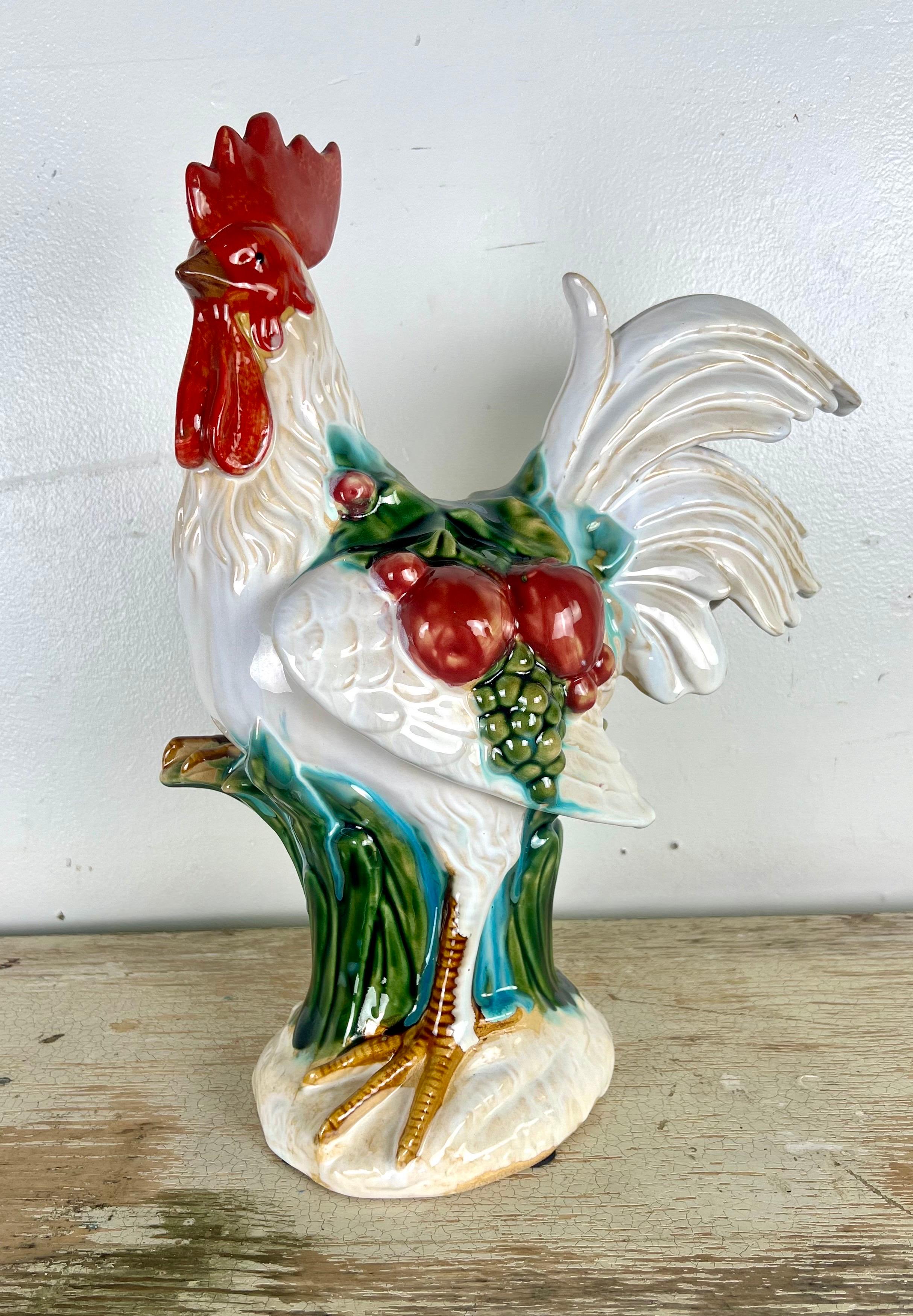 A quaint French glazed ceramic figure, a chicken that carries the charm of a rustic countryside kitchen.  This figure is meticulously adorned with an array of vibrant fruits; ripe apples and lush grapes are depicted in a palette of reds, greens,