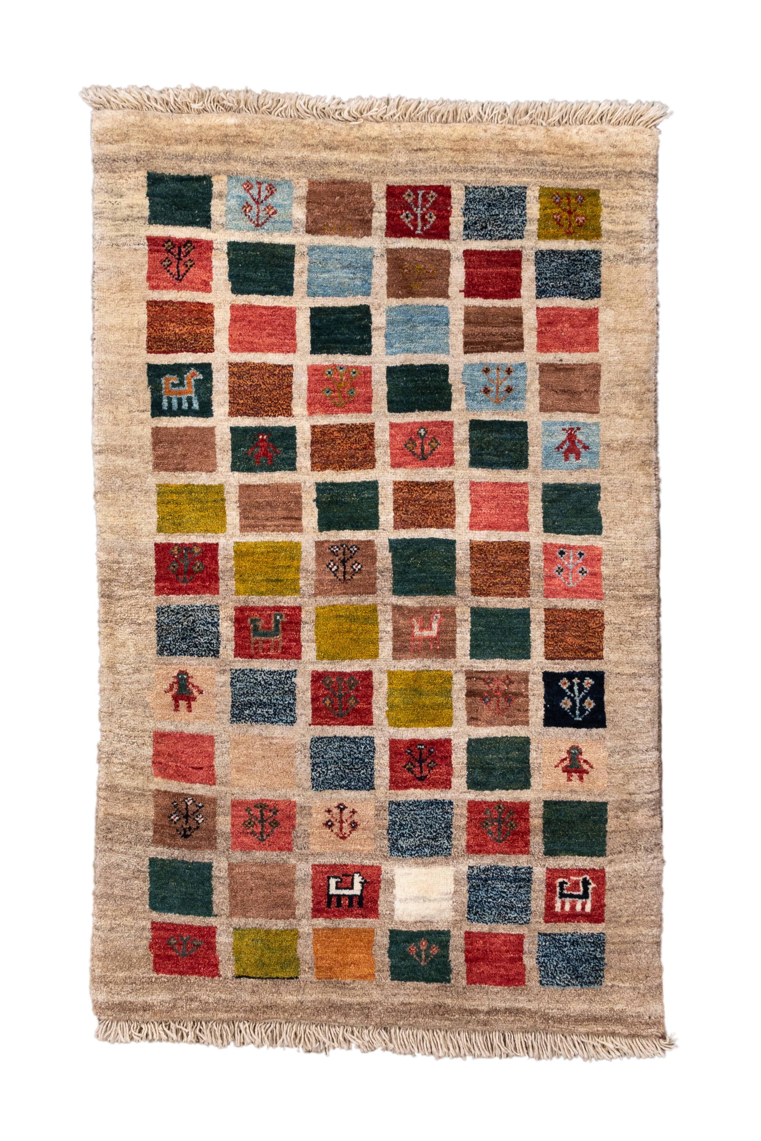 This charming tribal Gabbeh rug features a playful patchwork design of small squares in earthy and jewel-toned hues—green, indigo, rose, ochre, rust, ivory, and teal—each containing a tiny, hand-knotted motif. Stylized animals, trees, and abstract