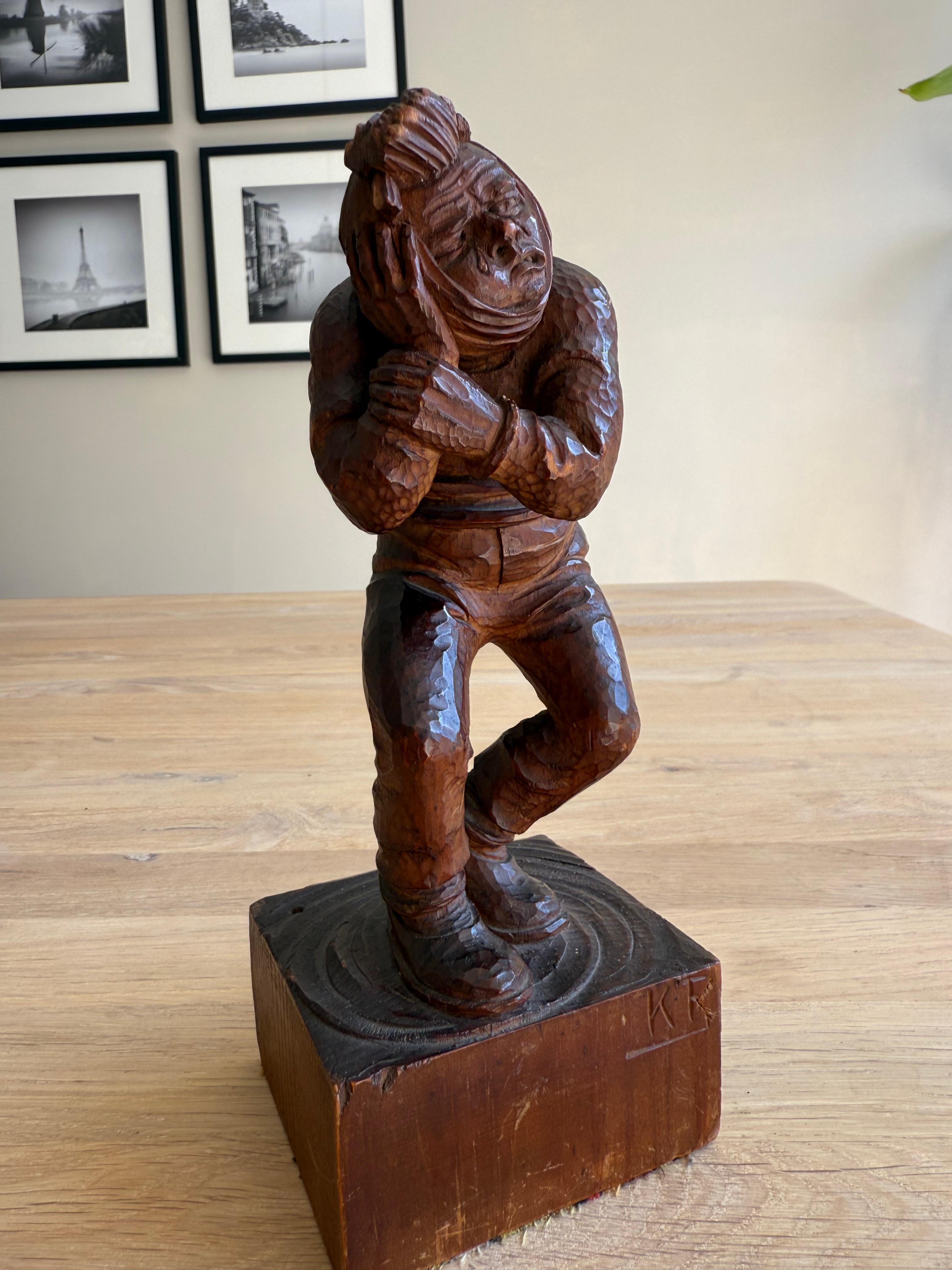 Mann mit Zahnschmerzen, Kopf in ein Tuch gewickelt.

Diese ausdrucksstarke und skurrile Holzskulptur fängt einen allgemein bekannten Moment ein: einen Mann, der unter Zahnschmerzen leidet. Die Figur beugt sich mit sichtbarem Unbehagen nach vorne und