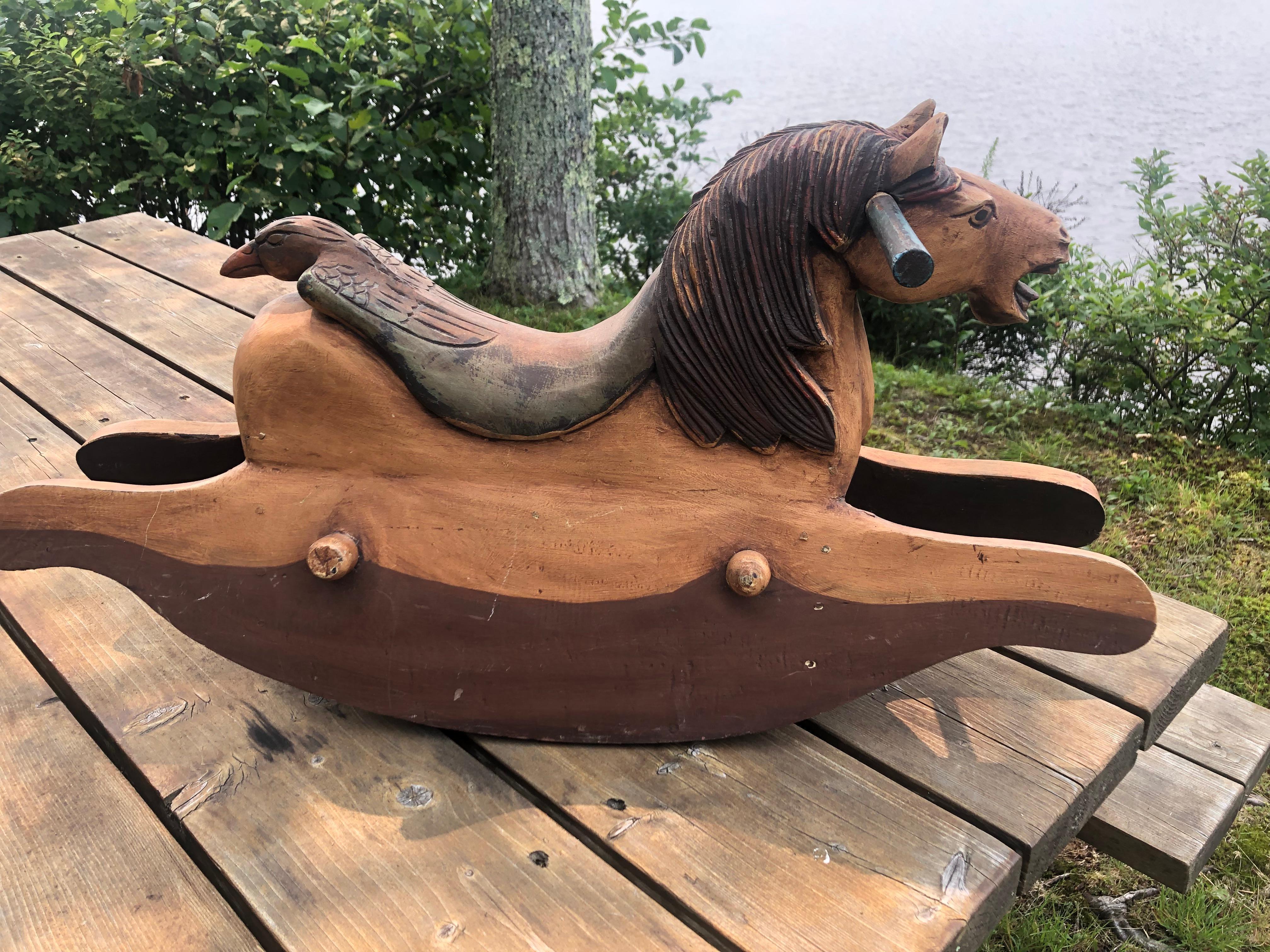 One of a kind hand carved rustic folk art sculpture of a rocking horse sourced in Maine, having wonderful facial expression with open mouth, meticulously detailed mane, and saddle that terminates on one side in the head of bird. Would make a