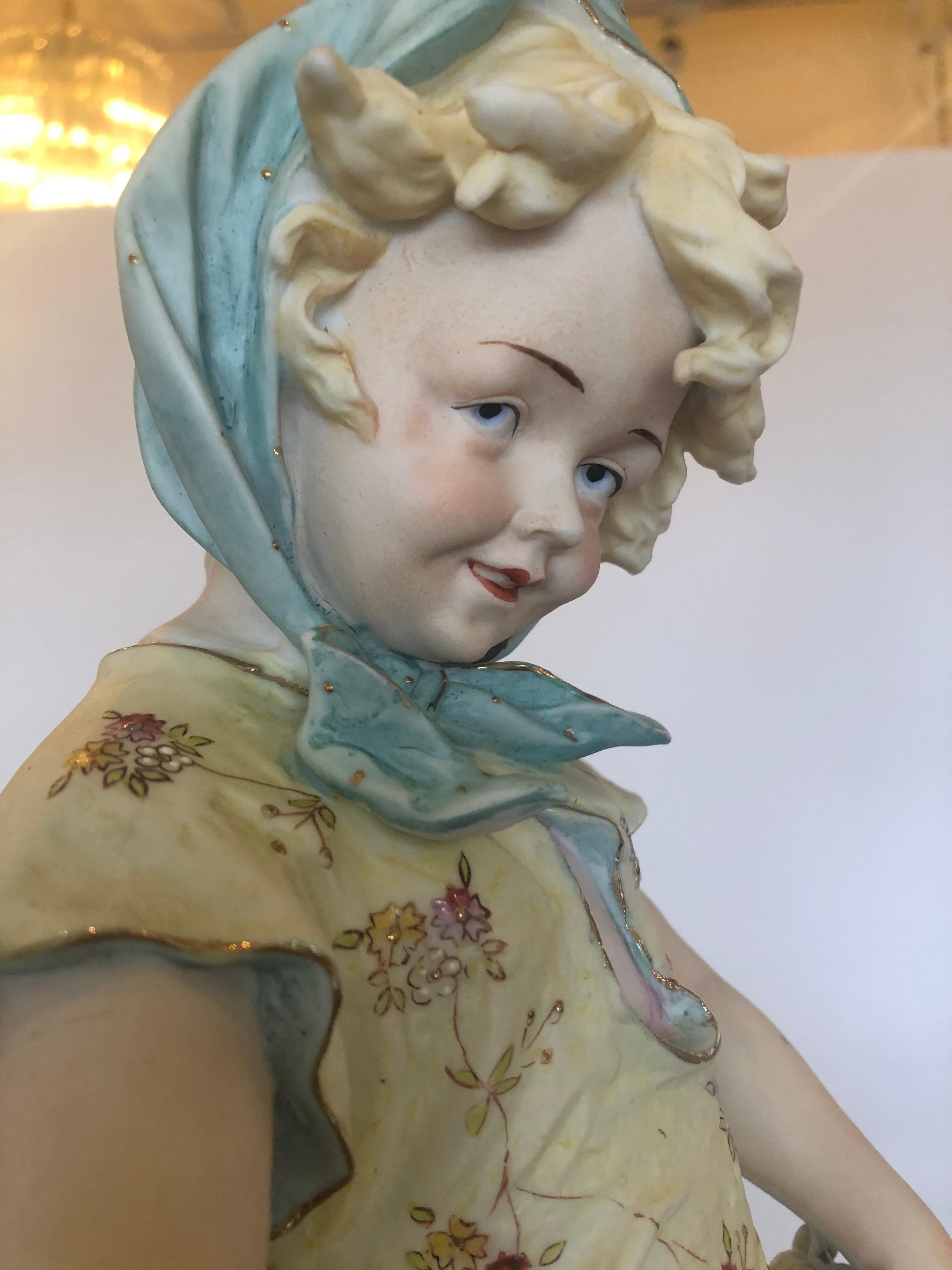 A tall meticulously detailed and hand painted parian porcelain figure of a country girl having blue bonnet and holding fruit in her apron. Signed on bottom.
