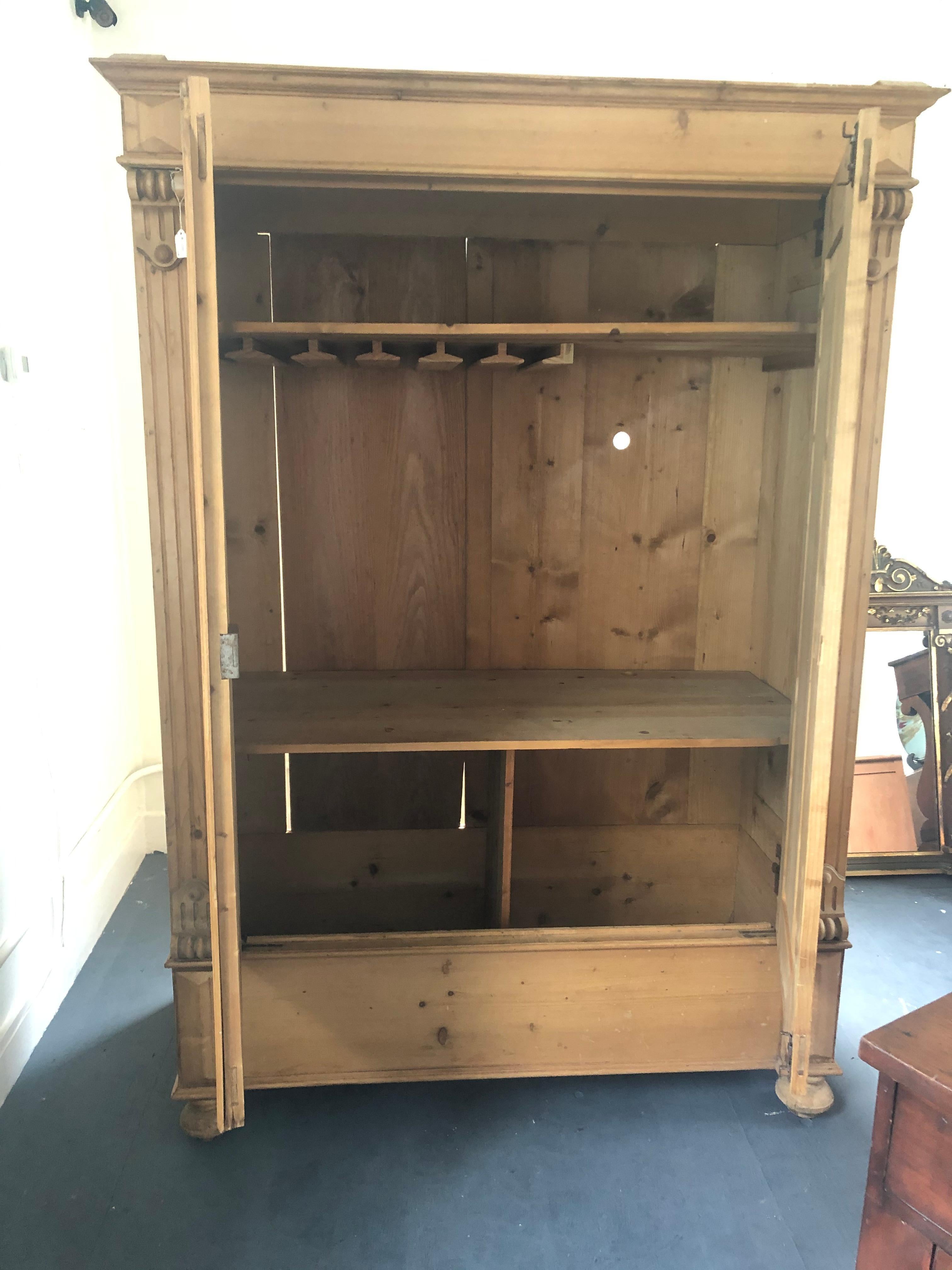 Wonderful and versatile antique German cupboard having natural pine construction and original brass hardware, round ball feet and beautiful carved wood decoration. Former owner outfitted the interior with wine glass rack so would make a fabulous dry