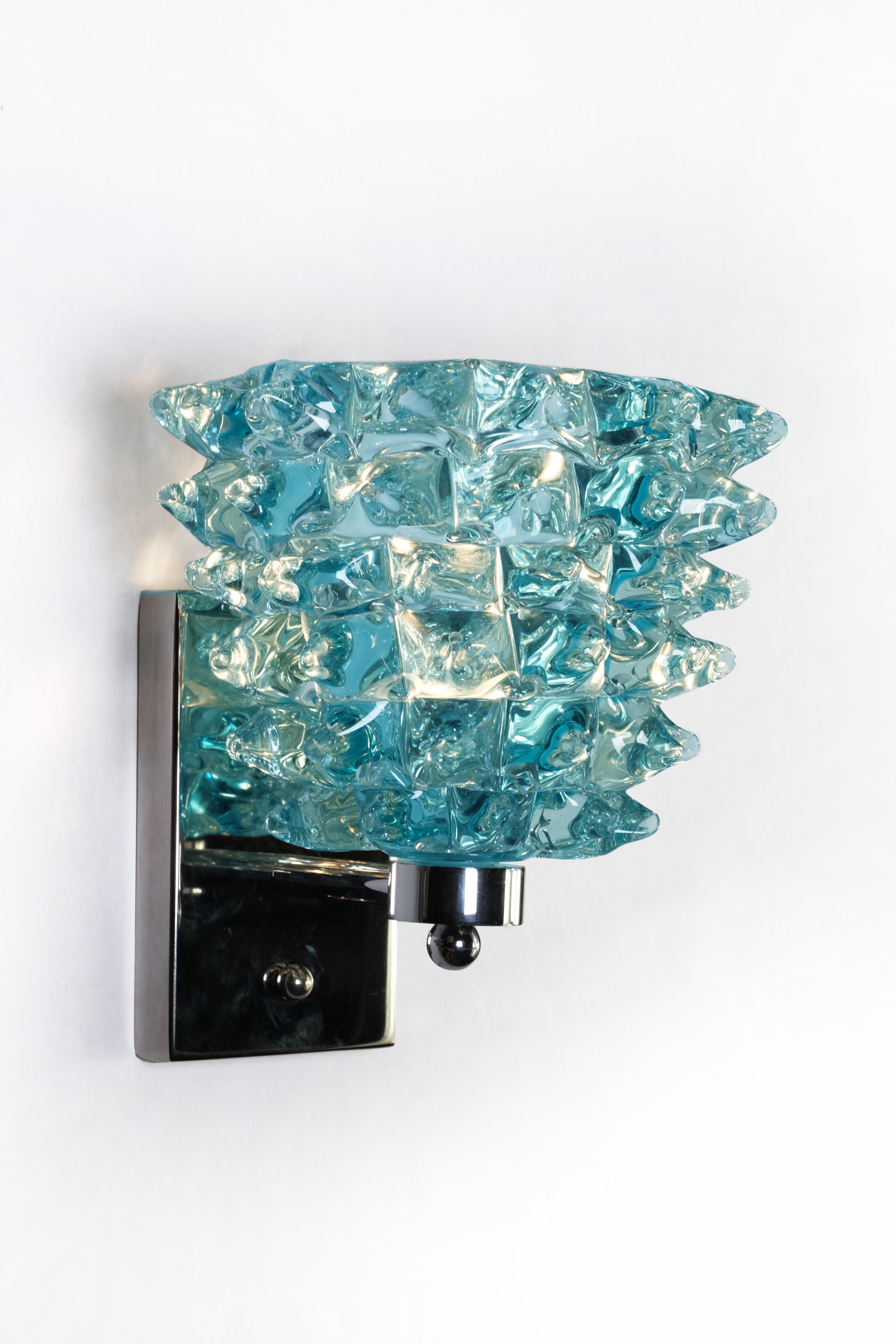 Designed to captivate and elevate, this exceptional pair of 1960s Italian wall sconces showcases a richly sculptural interplay of aqua Murano glass—each sconce meticulously hand-formed into dynamic, ice-like textures that shimmer with movement and