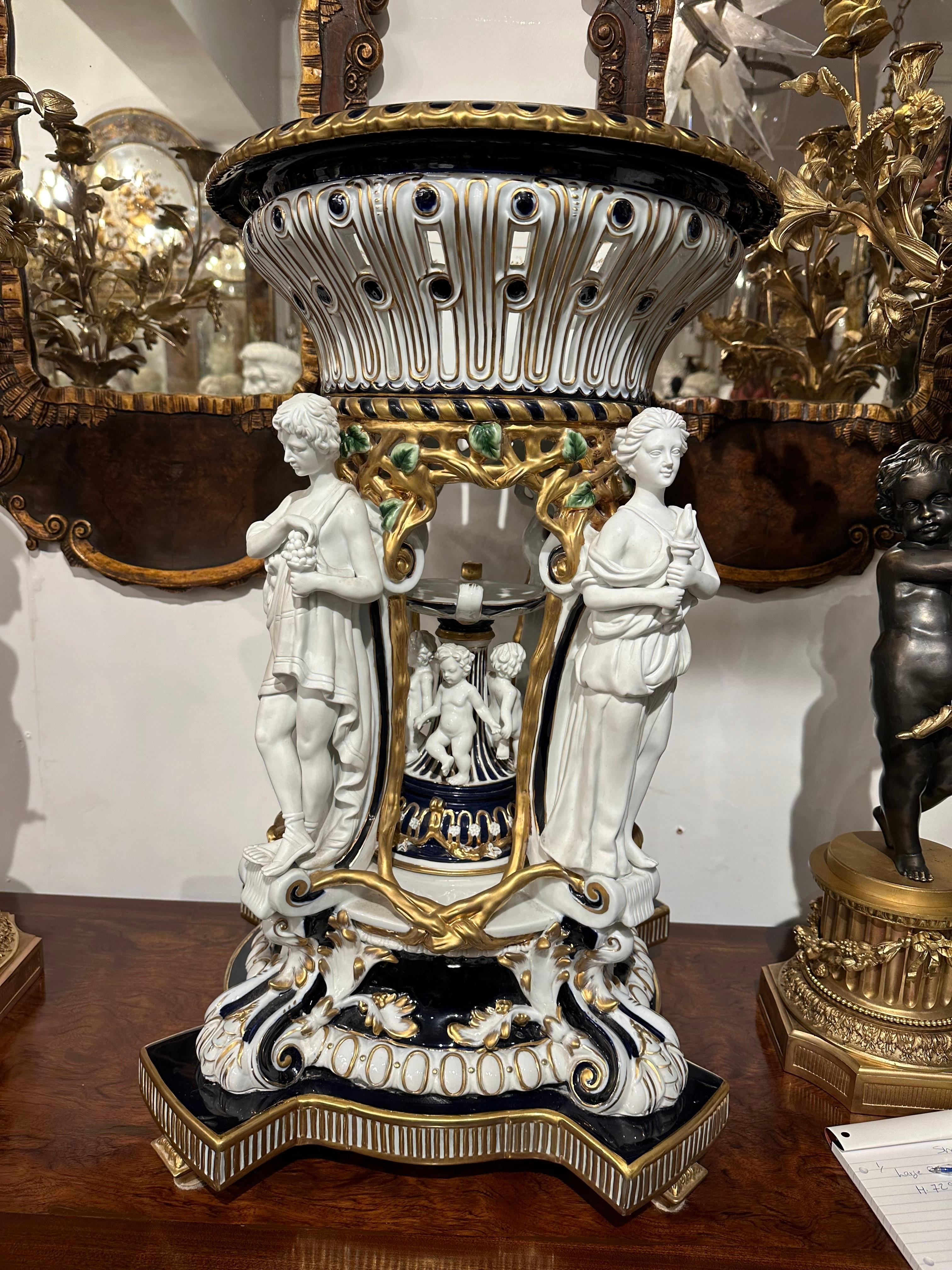 Charming large porcelain centrepiece of The four Seasons, with a pierced basket and delicate green foliage around the edge. Figures representing the Four Seasons stand on a rich deep blue, white and gold base encircling smaller cherurbs. The figures