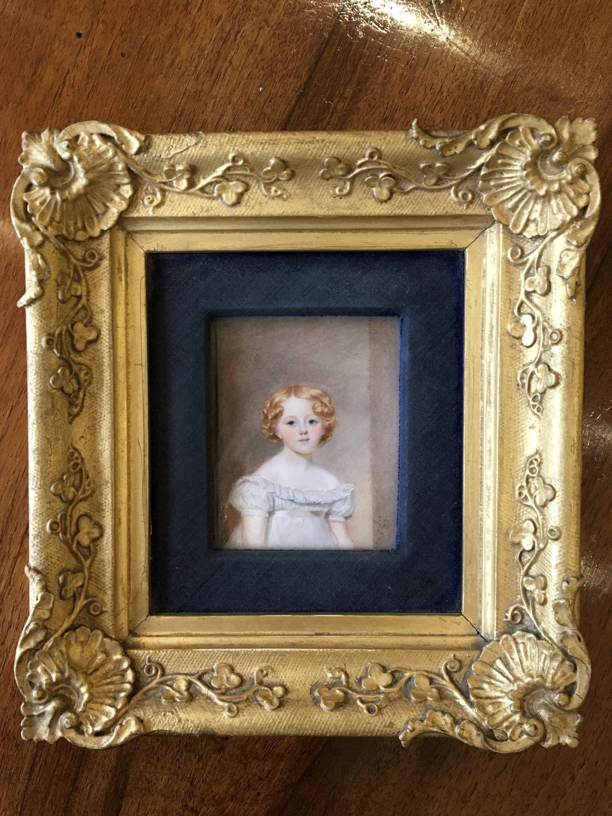 Portrait miniature: A girl, wearing white dress with frilled lace collar, satin waistband and short sleeves, her auburn hair center-parted and curled. Signed on the obverse with initials and dated T.L./ 1821, gilded composition frame, measures: the